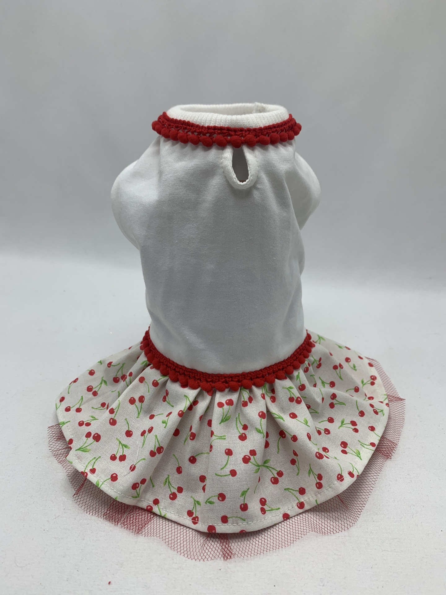 Vestido branco para cão com saia estampada de cerejas e detalhes em renda vermelha.