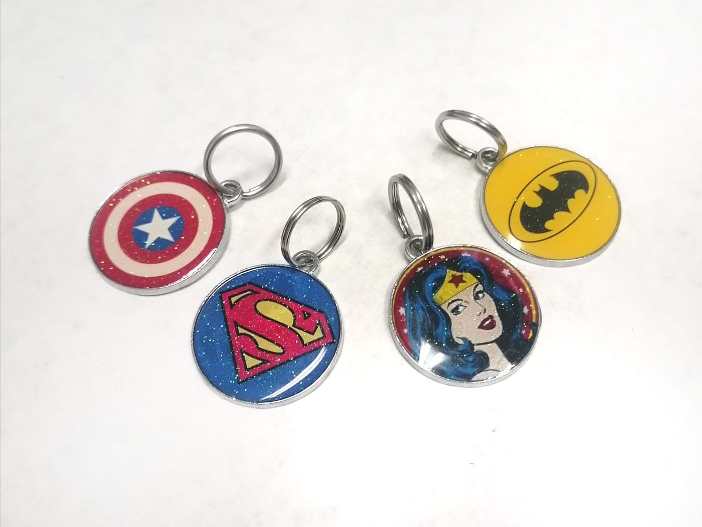 Quatro porta-chaves redondos com símbolos dos super-heróis Capitão América, Super-Homem, Mulher Maravilha e Batman