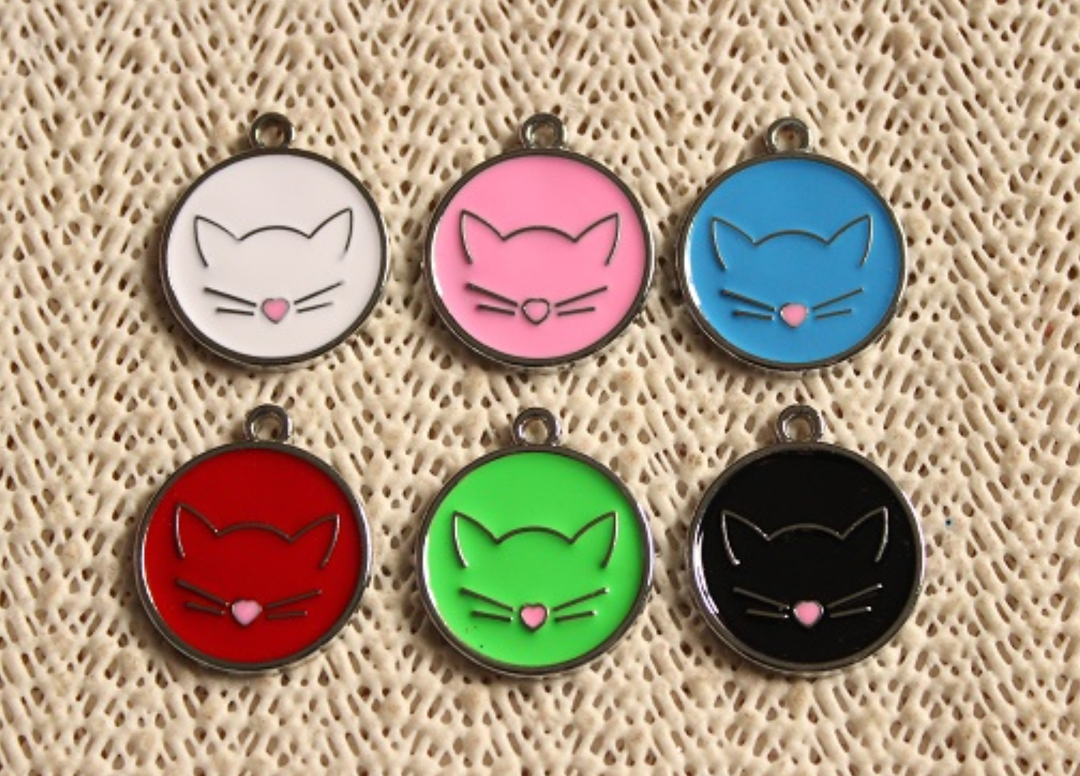 Seis medalhas redondas coloridas com desenho de gato sobre tecido bege