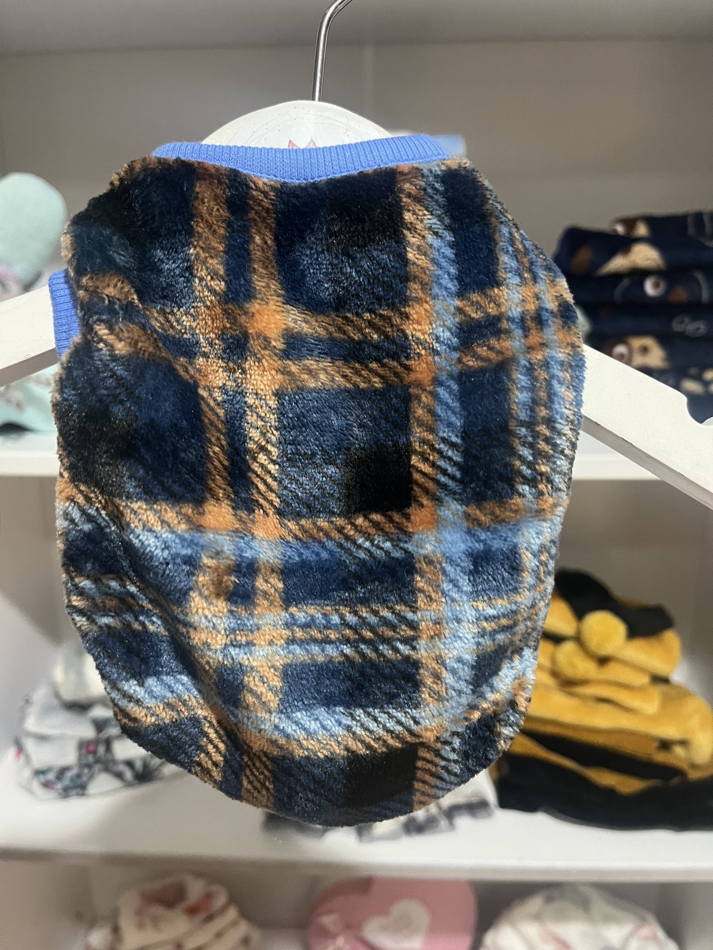 Casaco felpudo xadrez azul, castanho e preto para cão pendurado em cabide branco