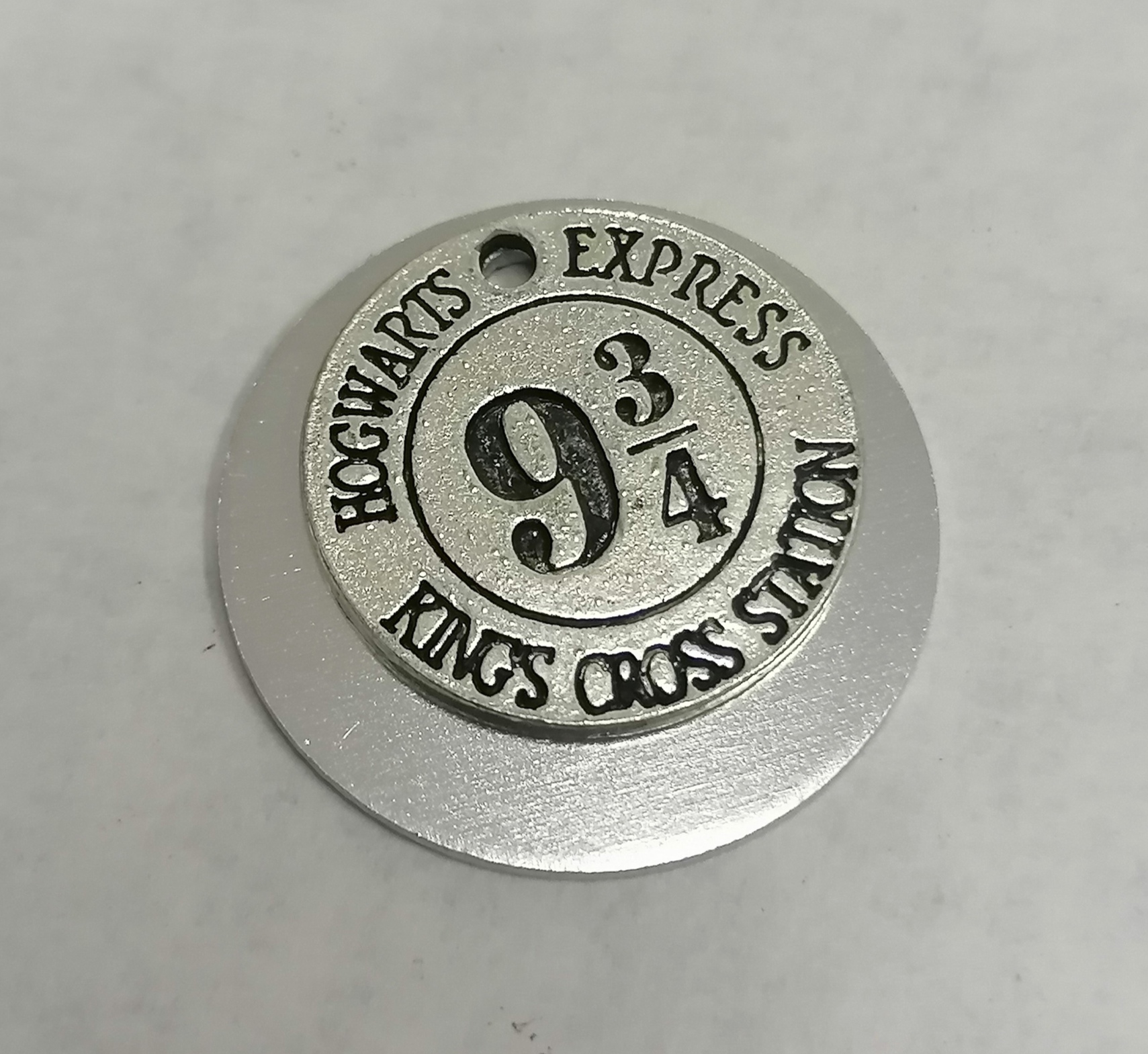 Medalha metálica prateada com texto Hogwarts Express 9 3/4 Kings Cross Station