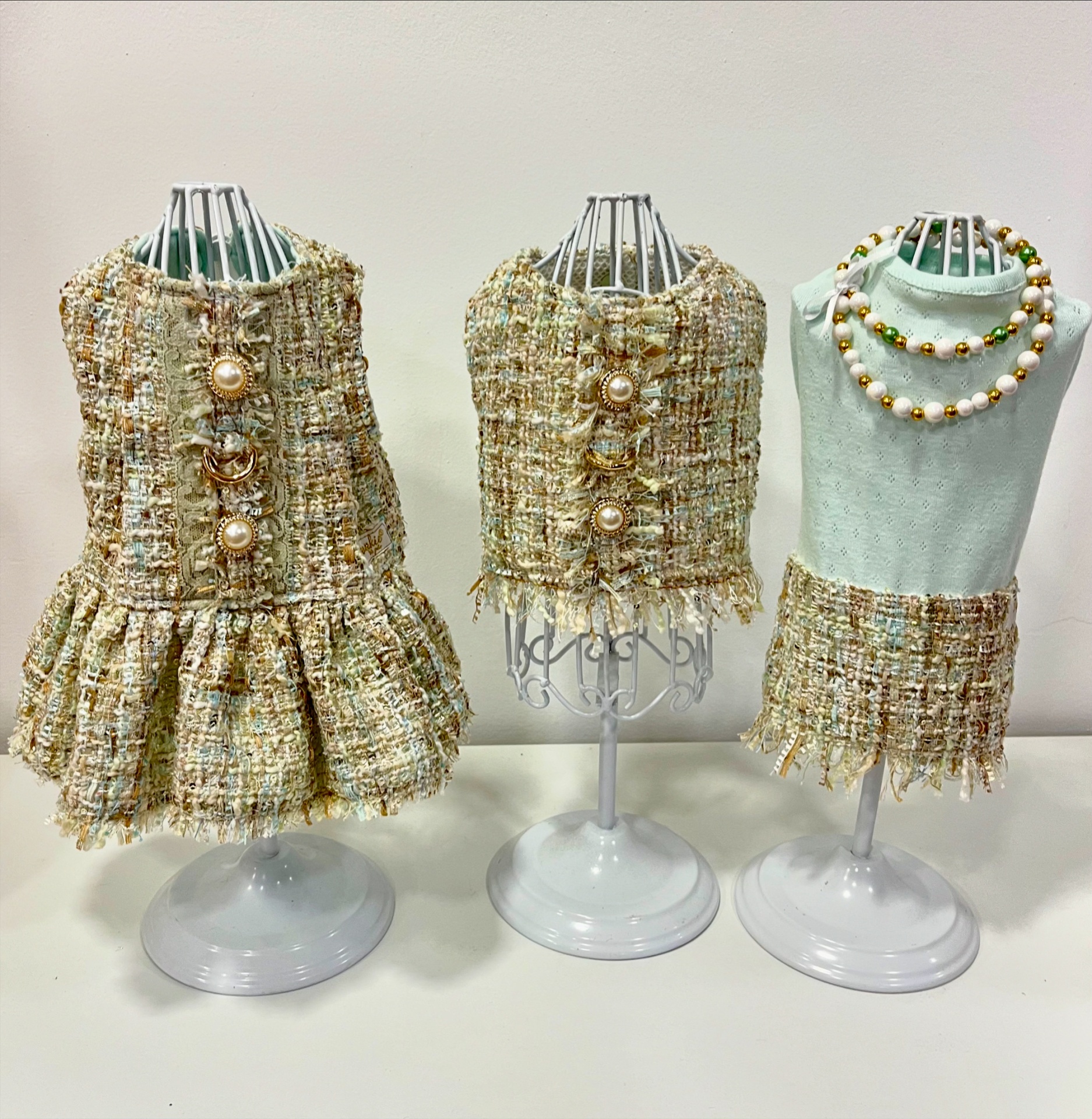 Roupas para cães em manequins com tecidos tweed e malha, acessórios de pérolas.