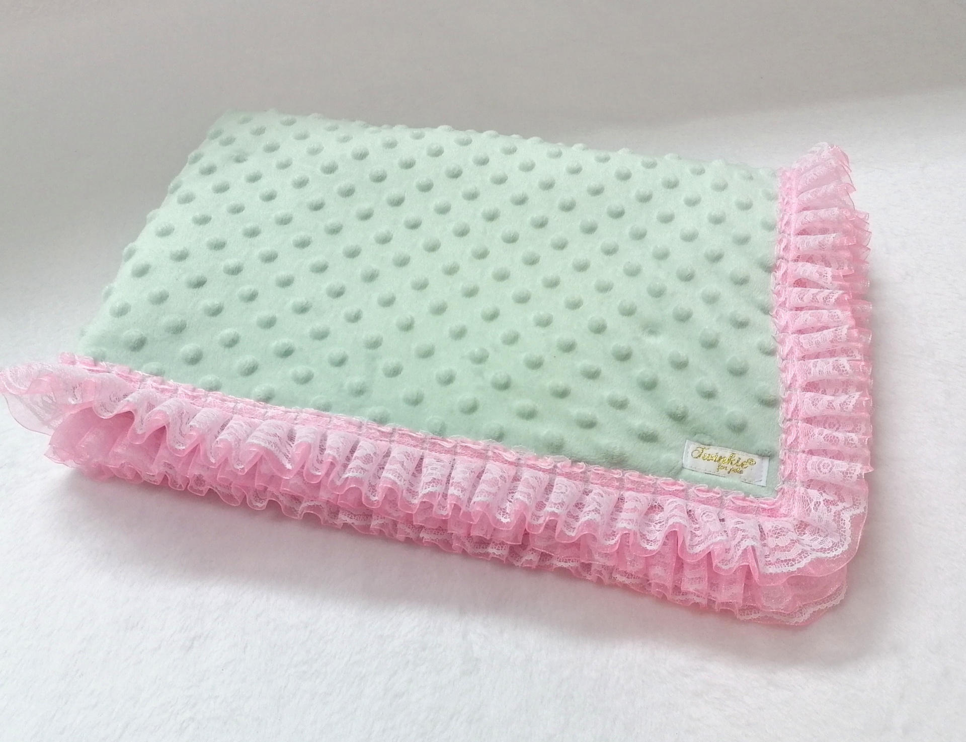 Manta verde clara texturizada com borda rosa rendada em fundo branco