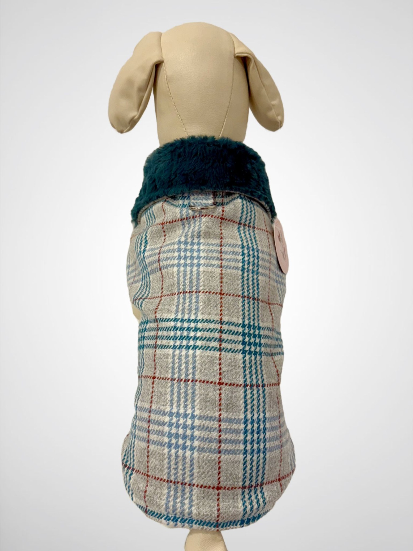 Casaco para cachorro xadrez bege, azul e vermelho com gola peluda azul escuro num manequim creme