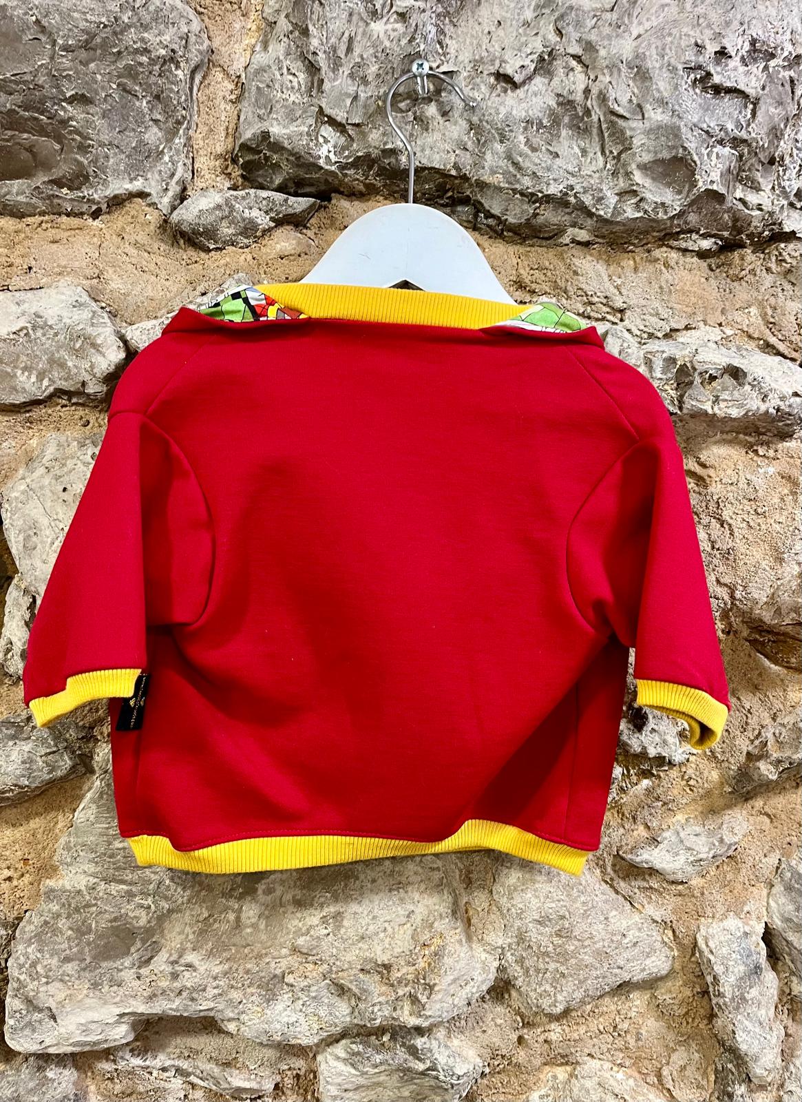 Camisola infantil vermelha com acabamentos amarelos pendurada num cabide branco