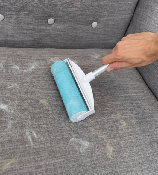 Rolo adesivo azul a remover pelos de sofá cinza.