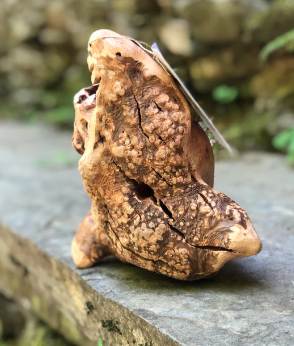 Escultura rústica em madeira com textura irregular sobre pedra