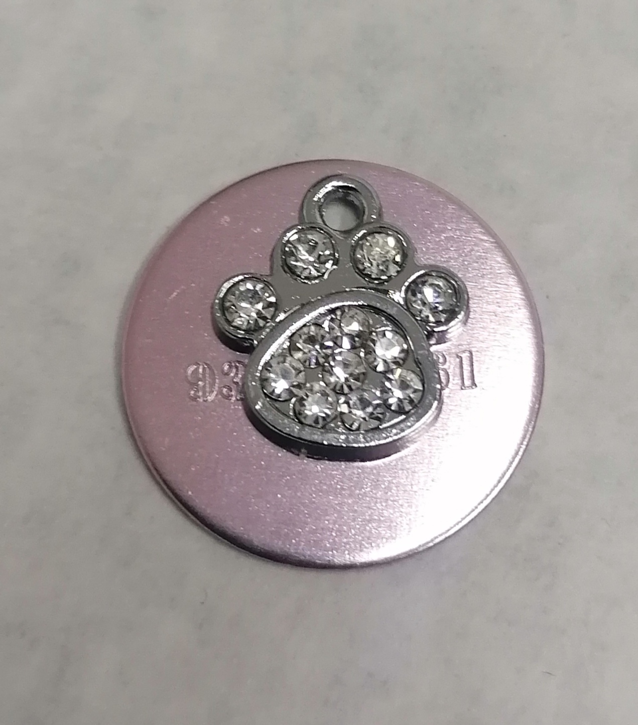 Pingente de pata de animal com pedras brilhantes sobre disco metálico rosa