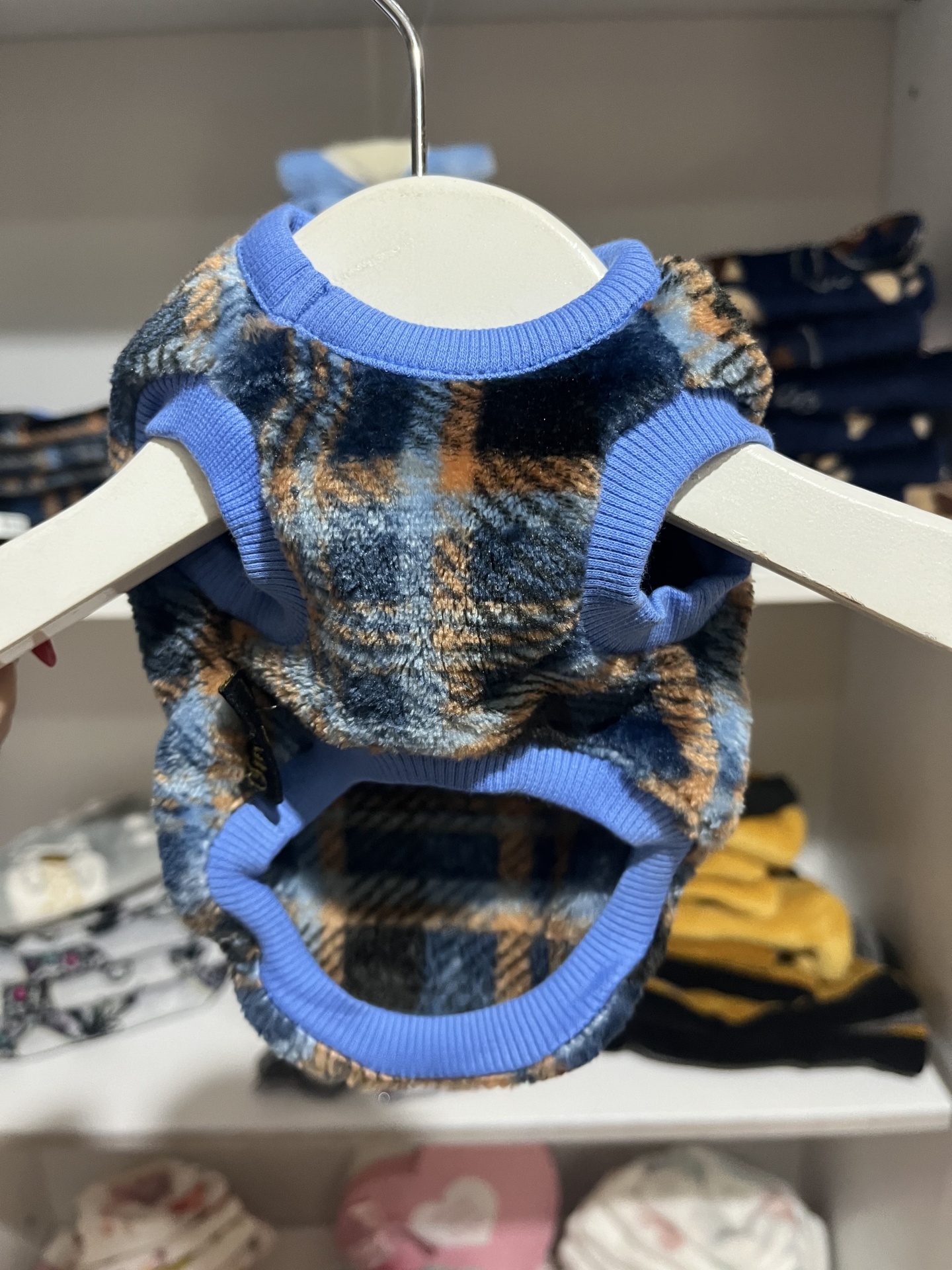 Roupa para animal com padrão xadrez azul, preto e castanho, bordas azul claro, pendurada em cabide branco