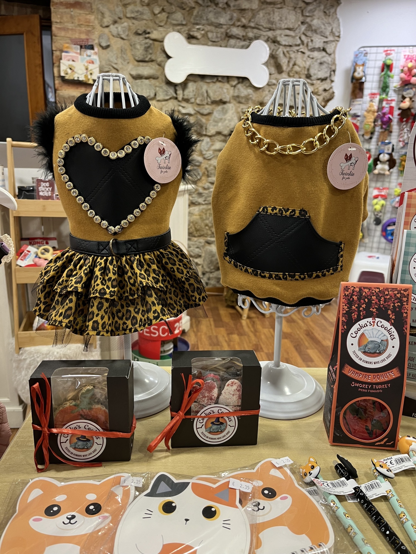 Dois fatos para cães em manequins com padrão leopardo e elementos decorativos, rodeados por acessórios para animais numa loja.