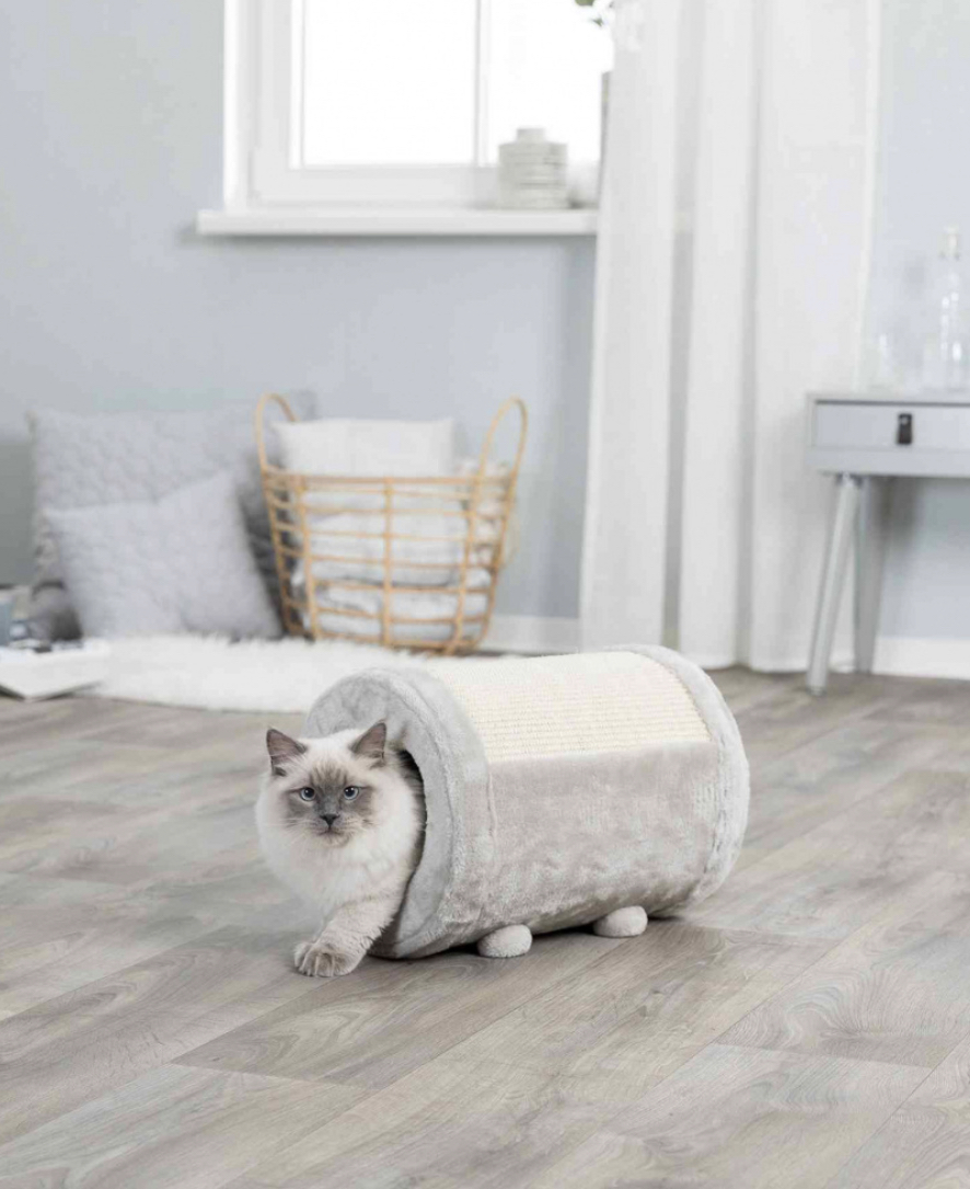 Túnel cinza claro para gatos com textura felpuda e topo rústico, gato branco saindo, em chão de madeira clara, ambiente doméstico com cesto e almofadas