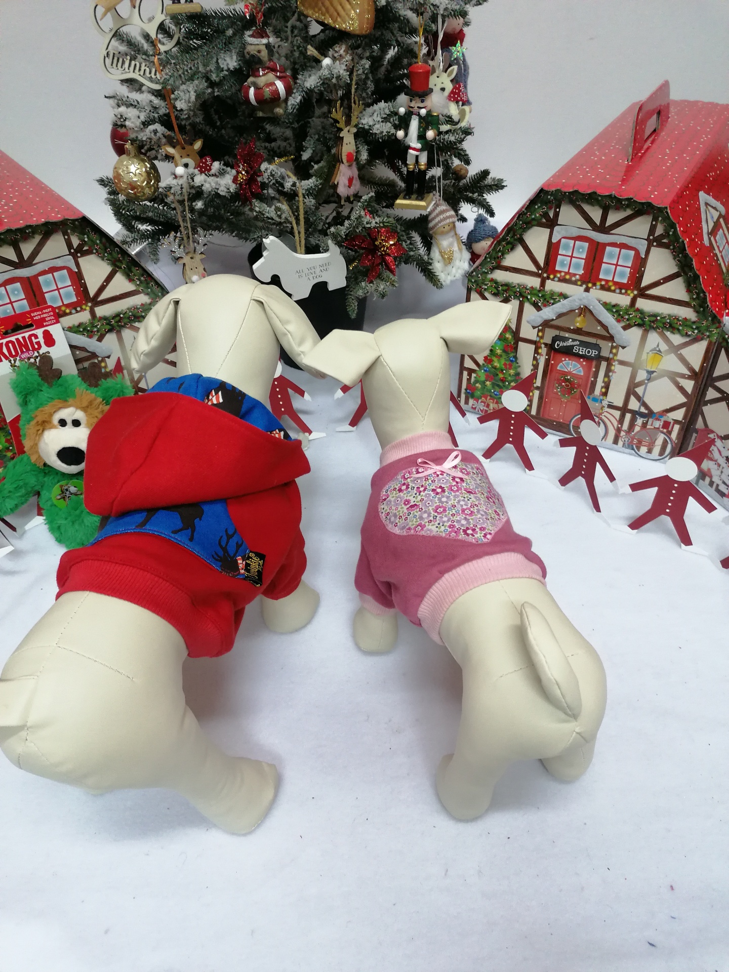 Dois manequins de cães com roupas vermelha e rosa com capuz, em cenário natalício