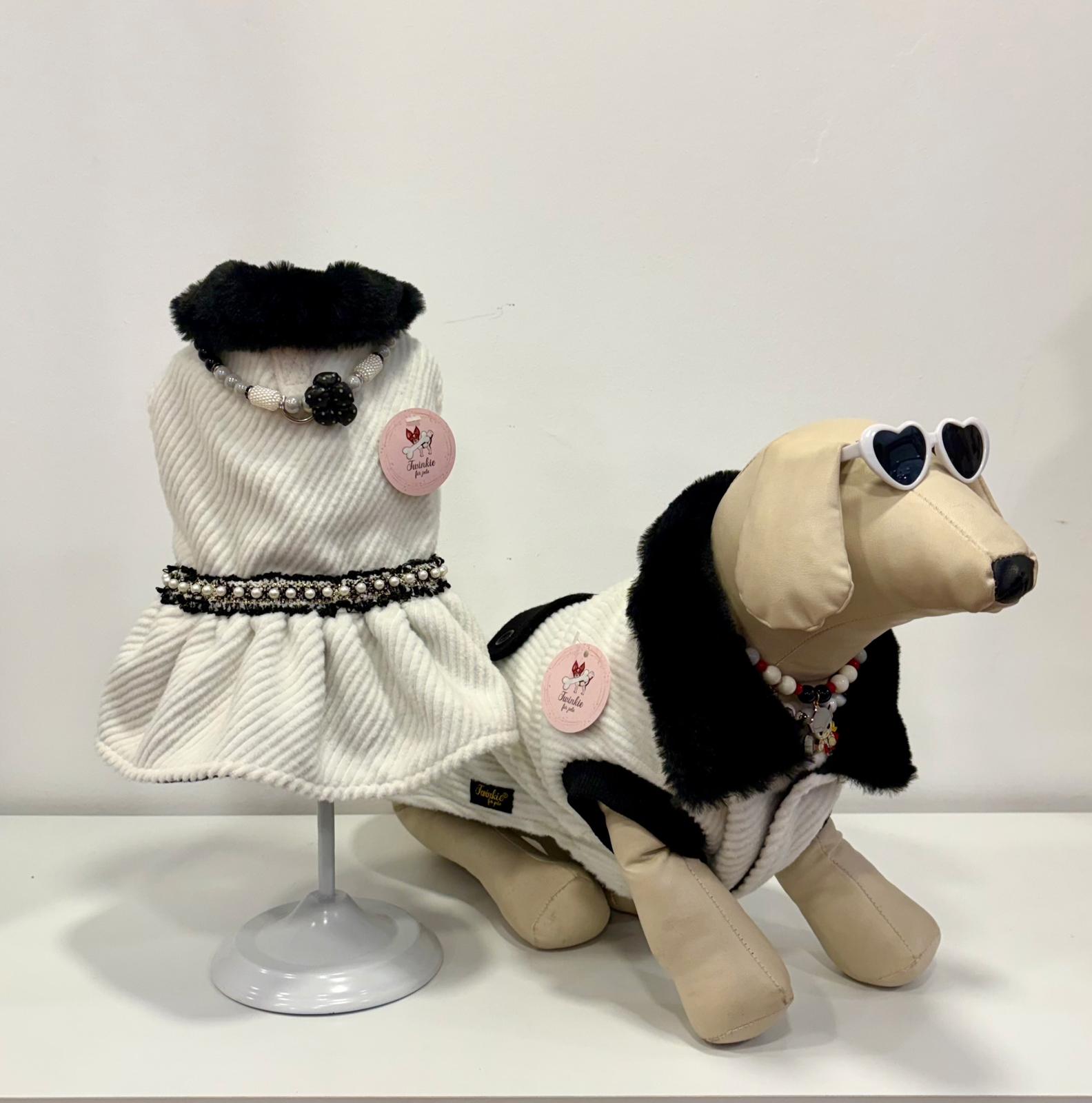 Dois casacos brancos com gola preta para cães, um vestido e um casaco, com etiquetas rosas Twinkle for pets, um manequim de cão com óculos em fundo branco.