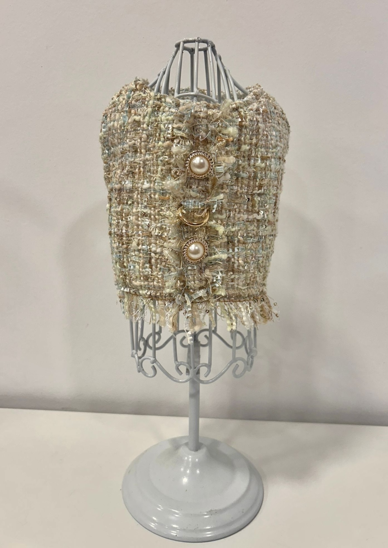 Top tweed bege com botões dourados e pérolas num manequim de metal