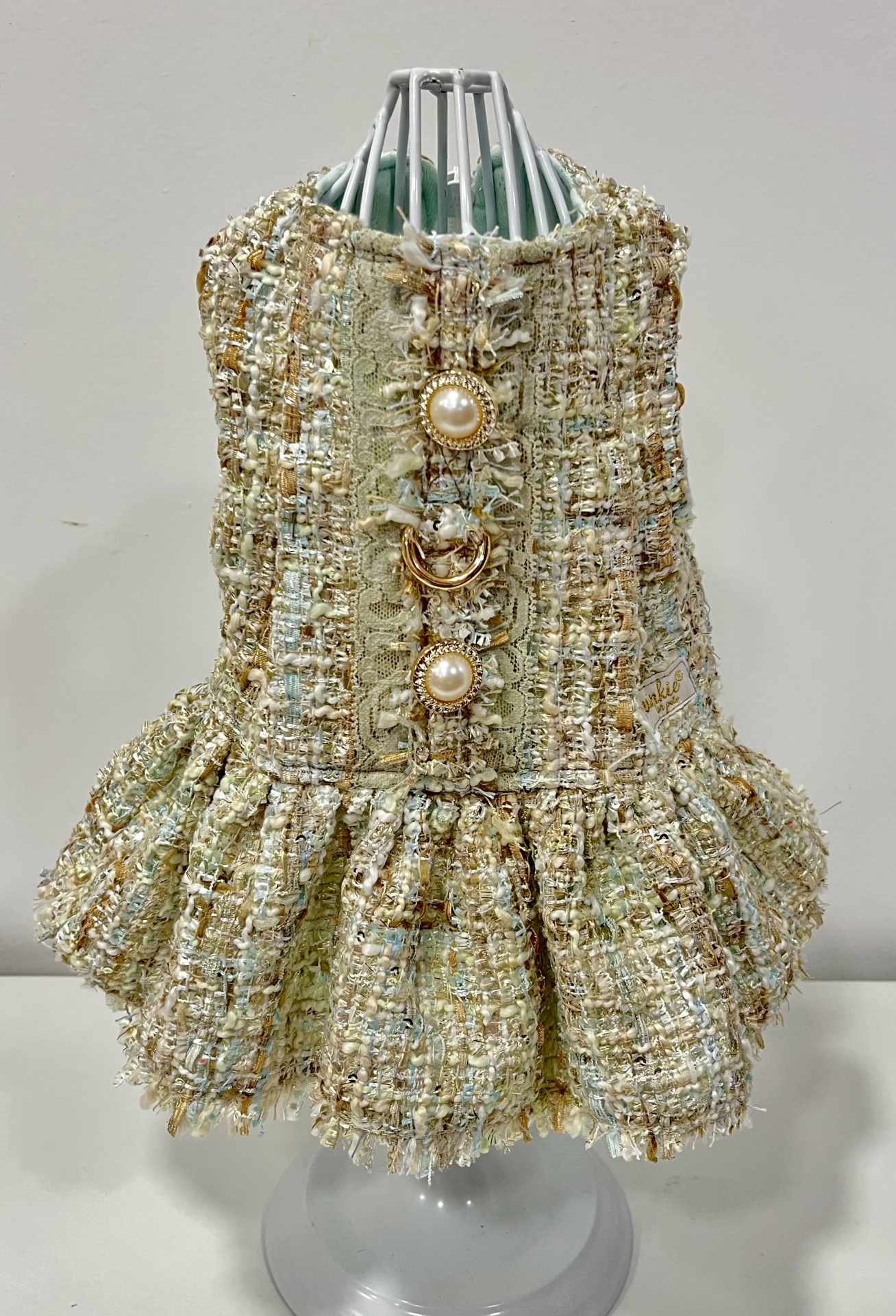 Vestido para cão em tecido tweed bege com botões de pérola e base plissada em manequim branco