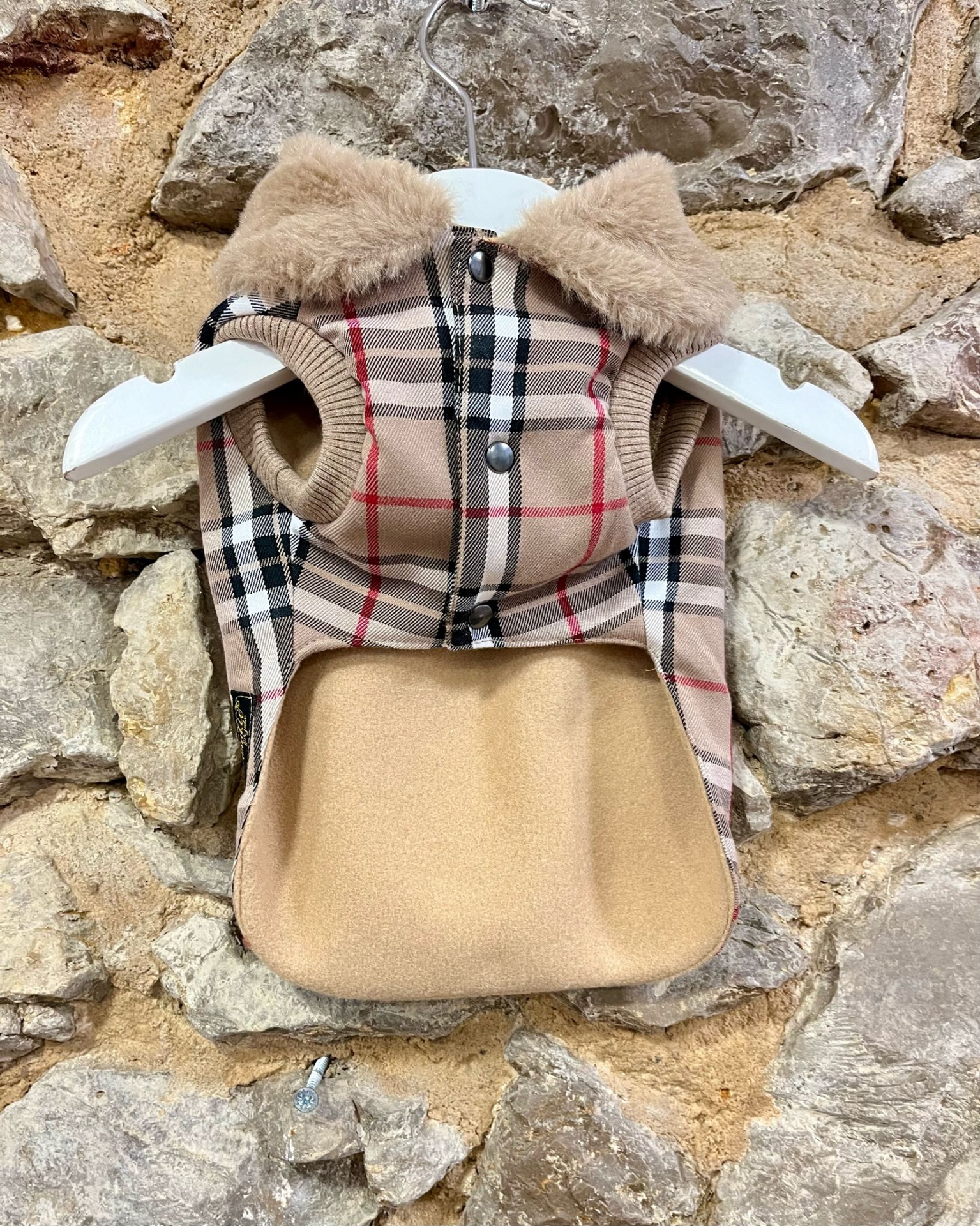 Casaco para animal de estimação em padrão xadrez com gola felpuda pendurado em cabide branco