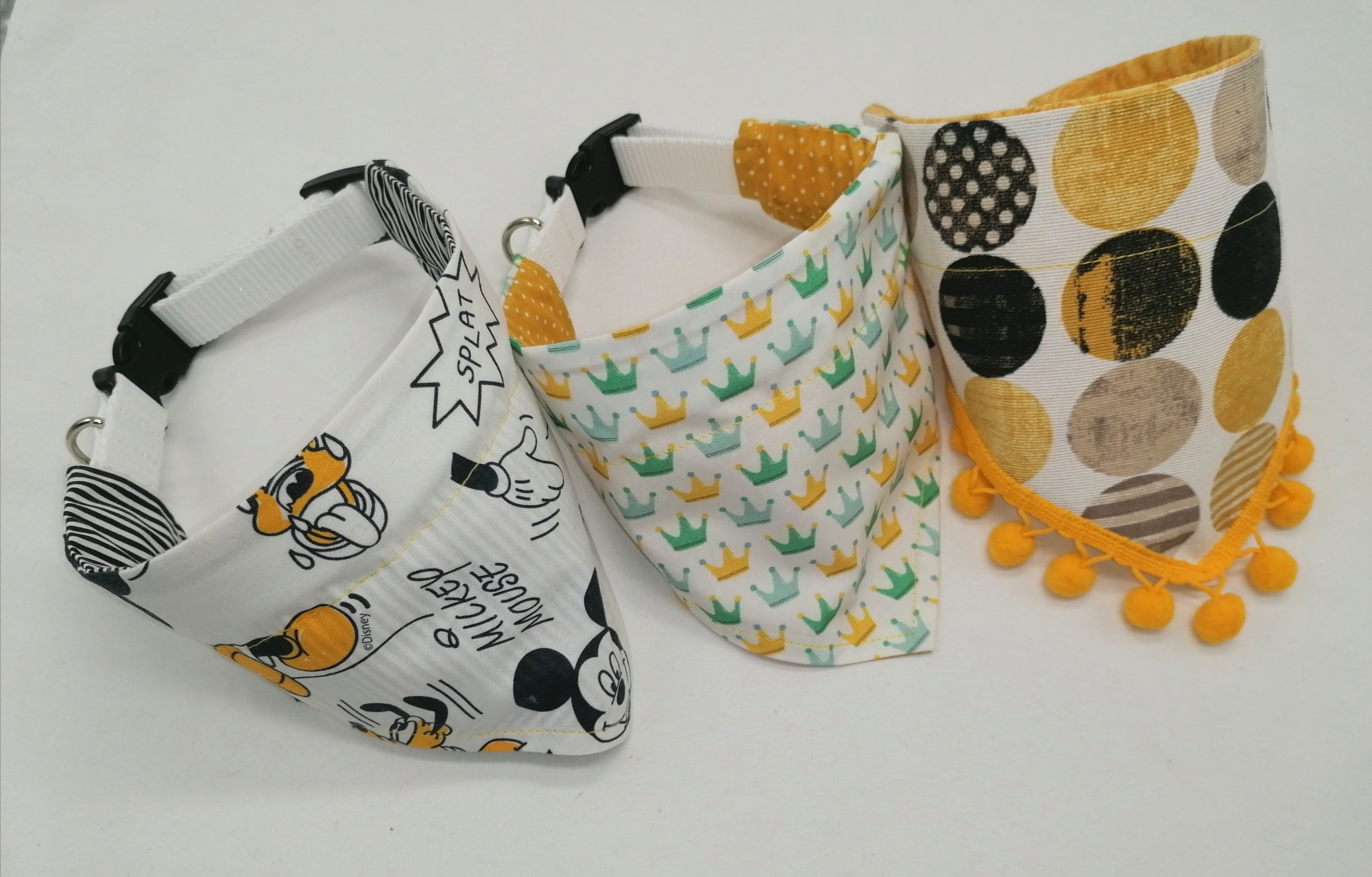 Três babetes triangulares coloridos com estampados e pompons