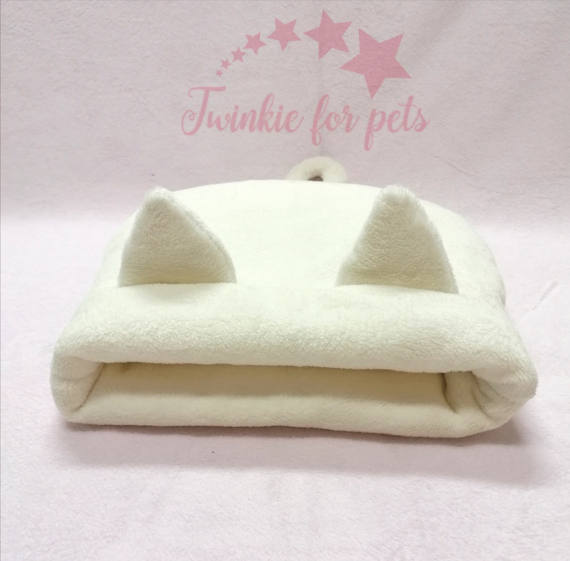 Cama felpuda branca para animais de estimação com orelhas, sobre tecido rosa e texto 'Twinkie for pets'.