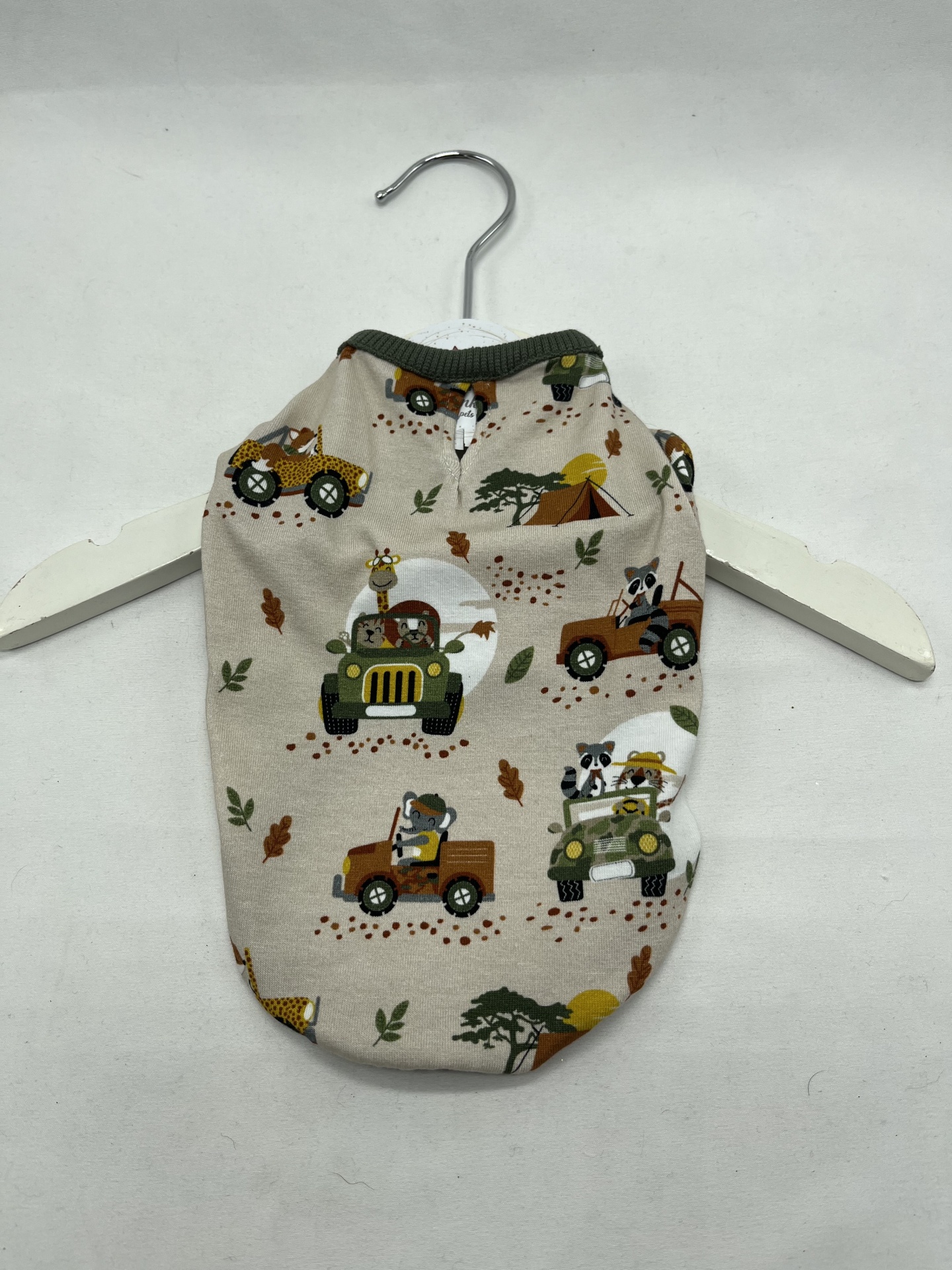 Roupa para cachorro bege com padrão de carros de safari e animais, pendurada em cabide branco