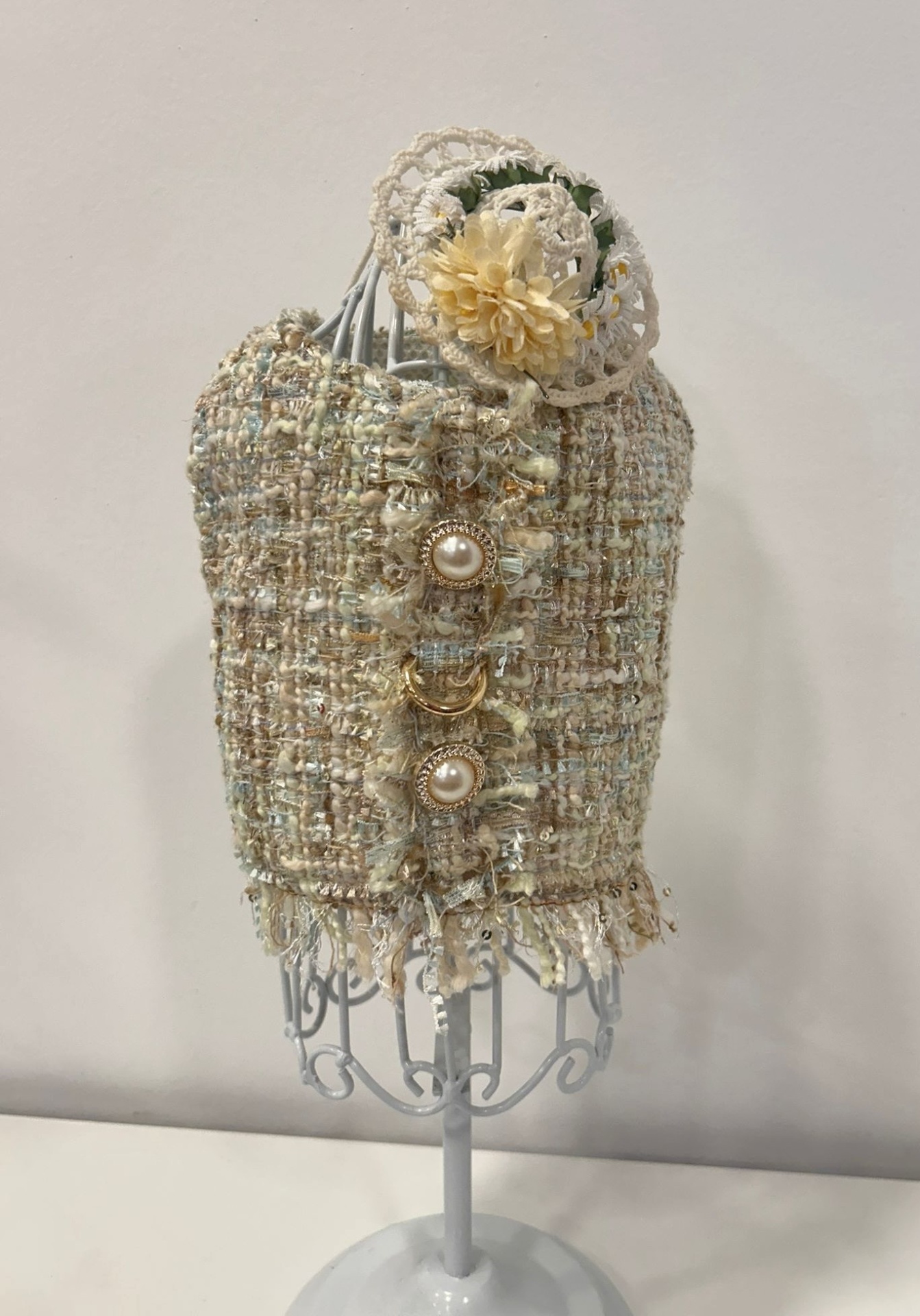 Colete tweed bege com botões perolados e renda branca em manequim metálico branco