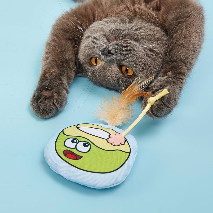Gato cinzento a brincar com brinquedo redondo com estampa de coco verde e penas