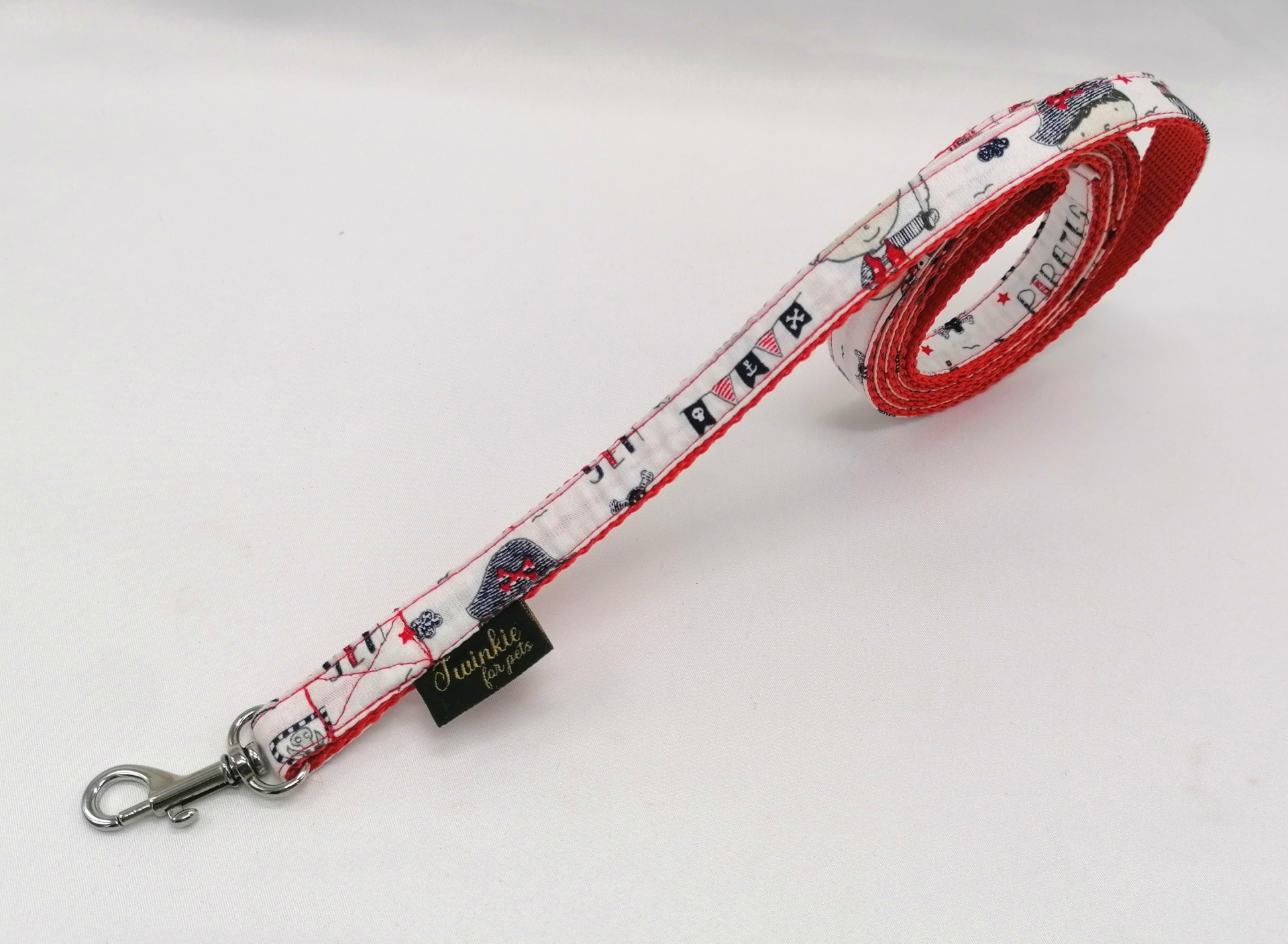 Trela para cão com padrão branco, vermelho e azul e gancho metálico.