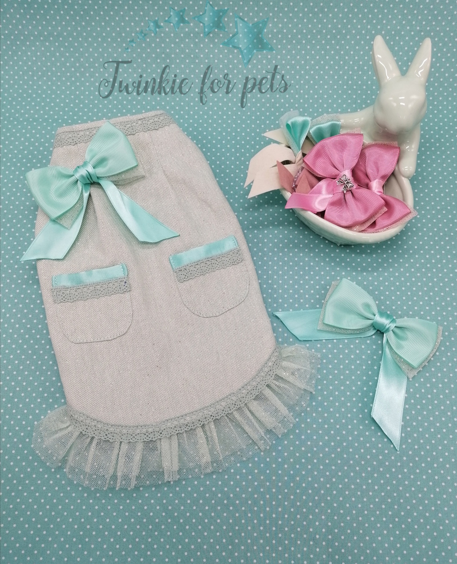 Roupinha para cão bege com laço azul-claro, dois laços decorativos e figura branca de coelho sobre fundo azul com bolinhas brancas