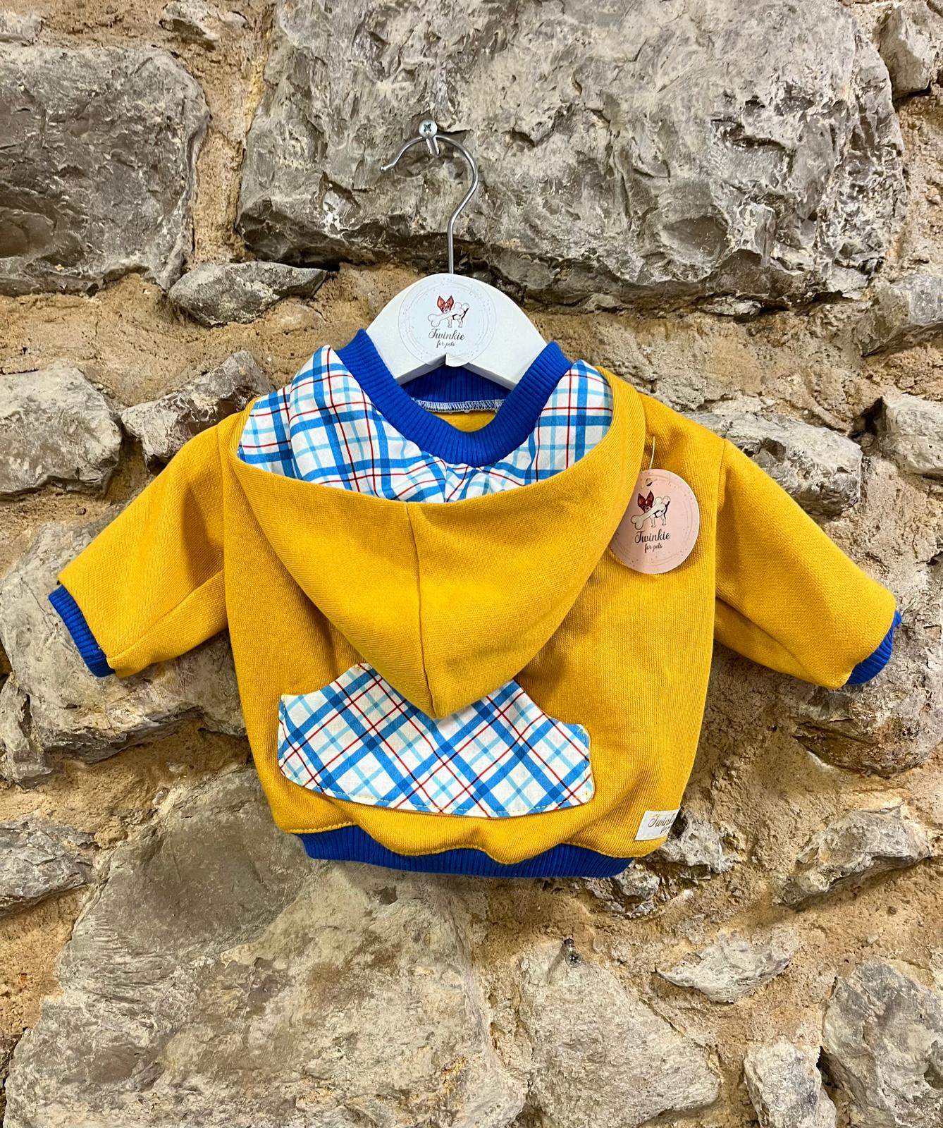 Casaco amarelo com detalhes xadrez pendurado em cabide branco contra parede de pedra