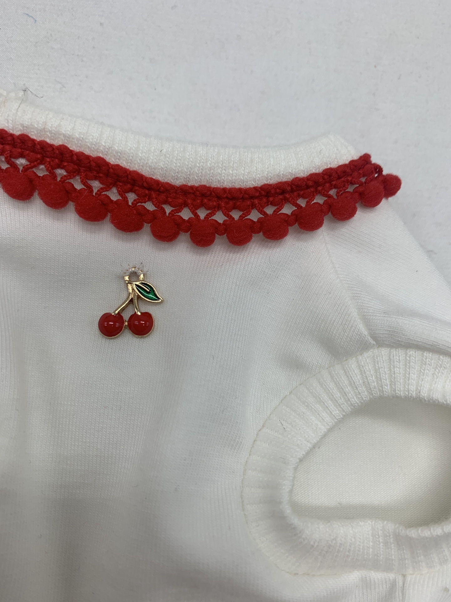 Peça de roupa branca com bordado vermelho e pendente de cereja