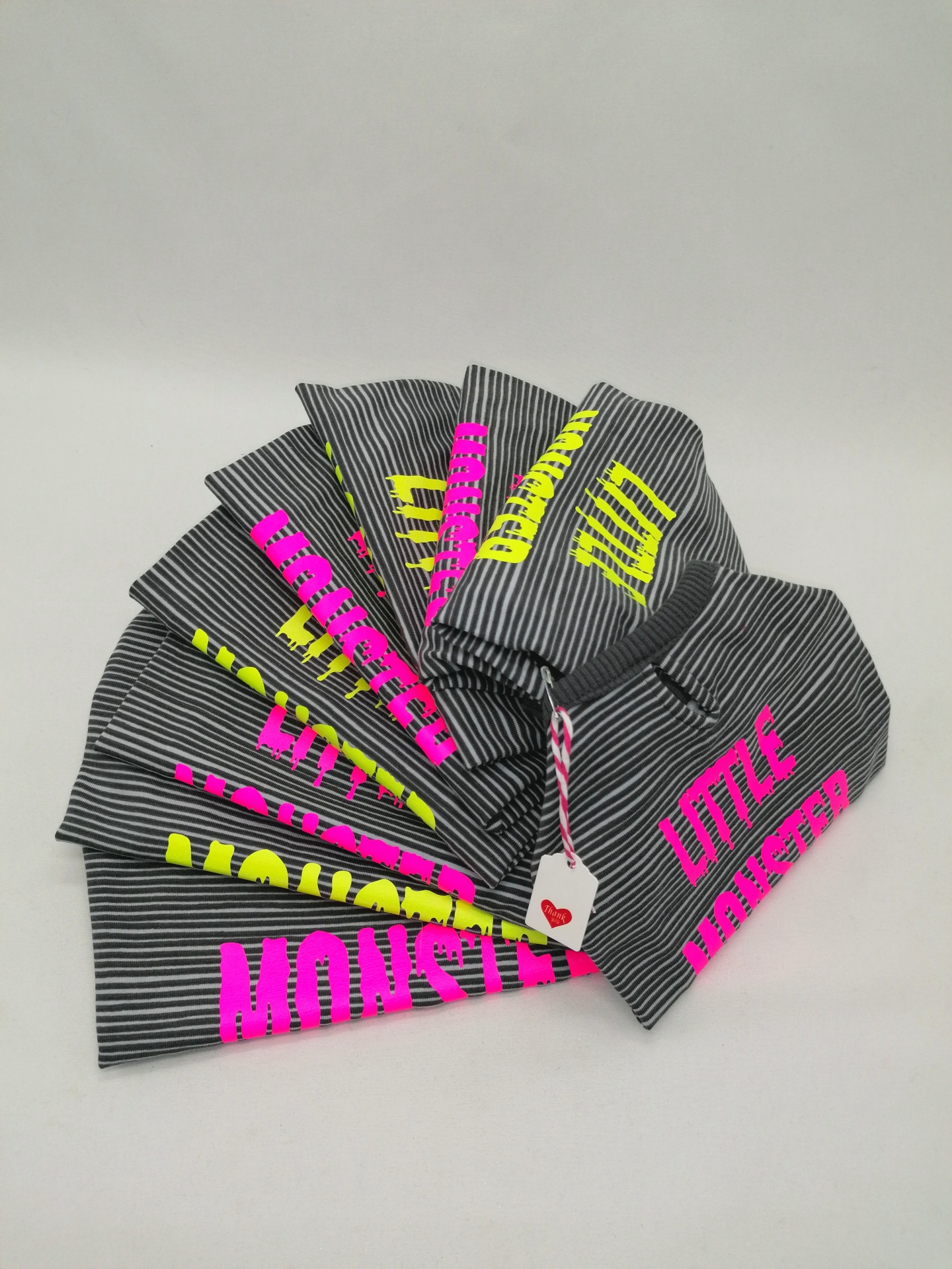 Gorros cinzentos com riscas e texto 'LITTLE MONSTER' em rosa e amarelo.