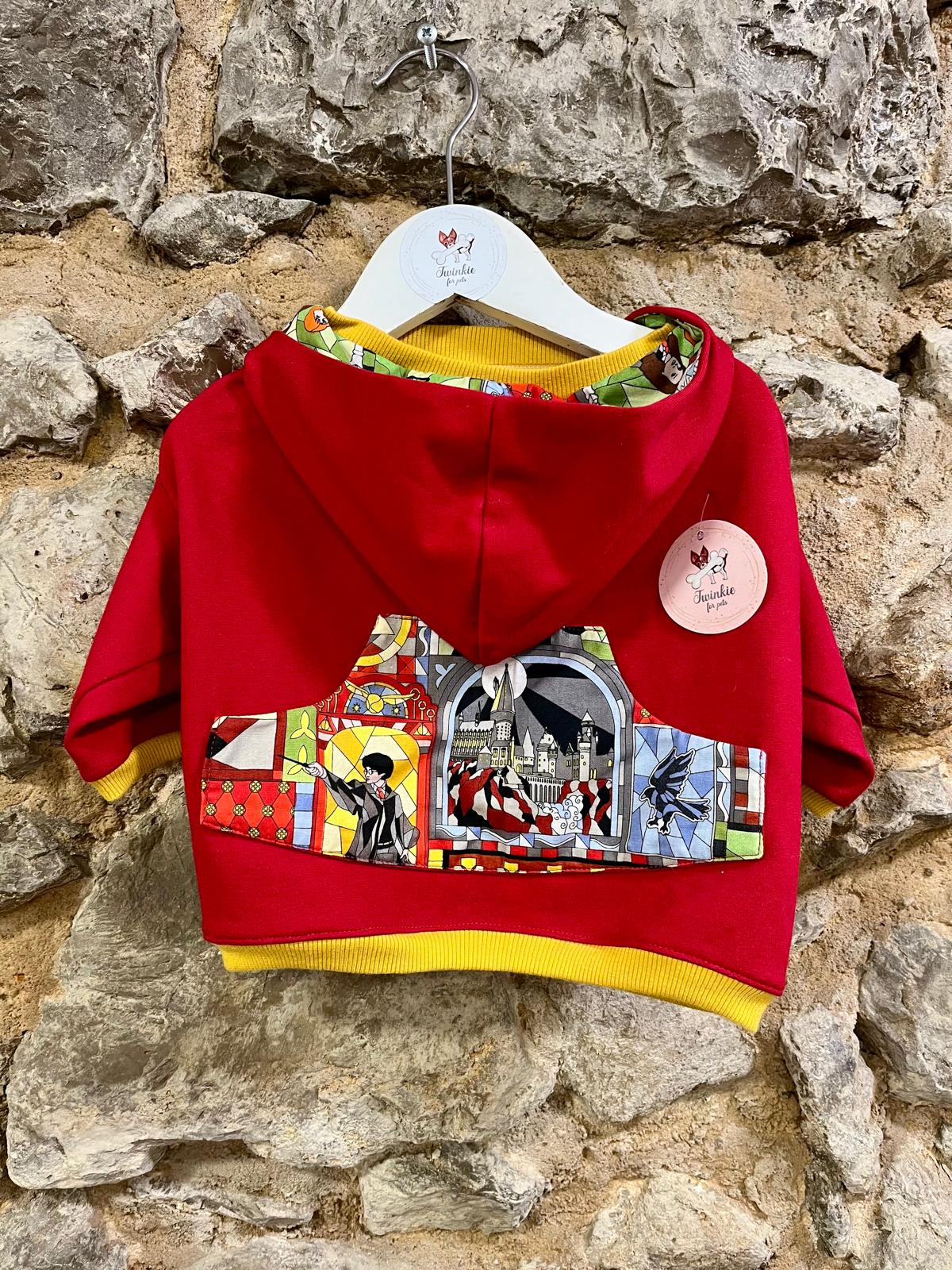 Casaco vermelho com capuz e estampas coloridas pendurado numa parede de pedra