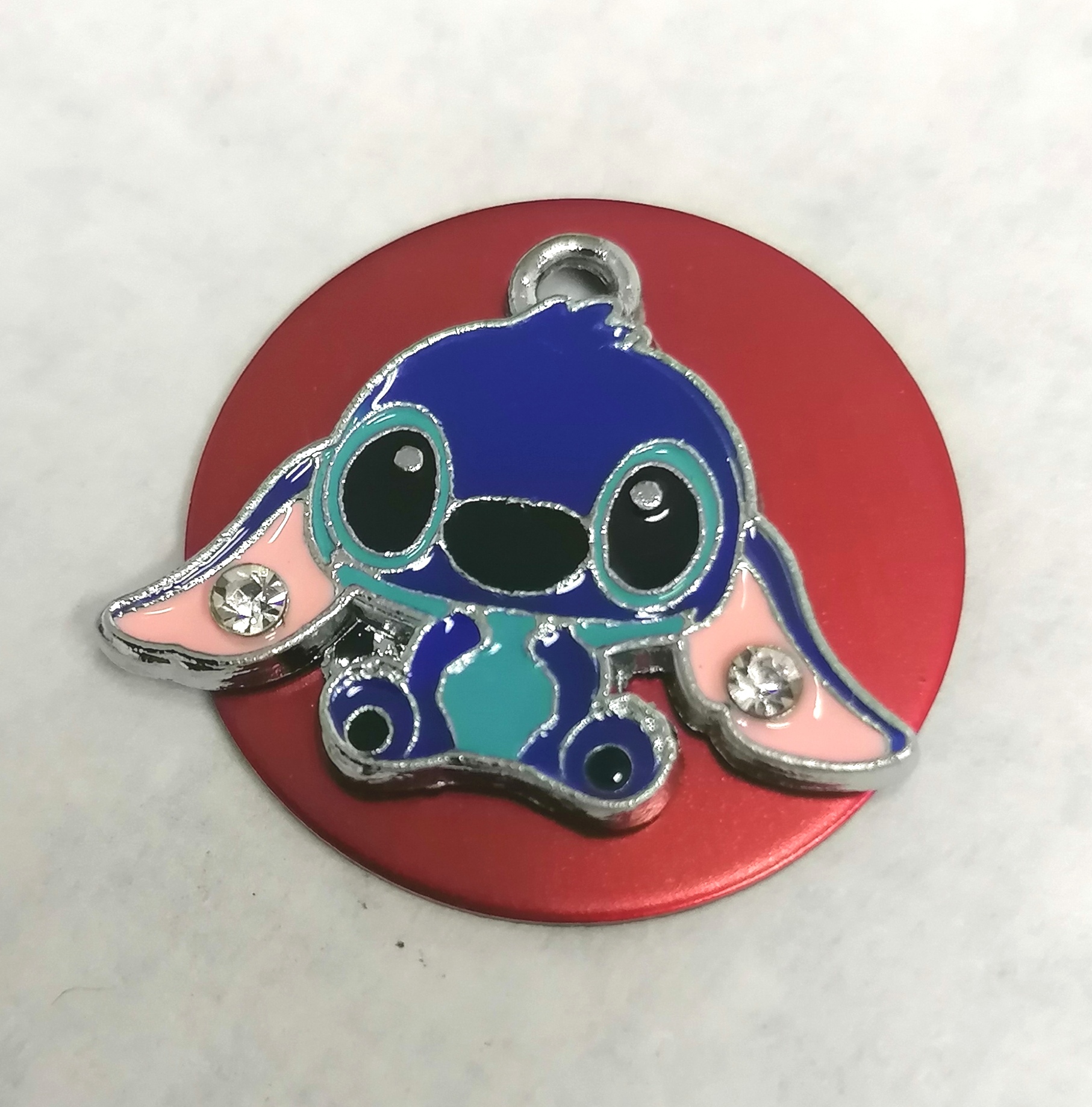 Pendente de Stitch colorido com duas pedras brilhantes sobre disco vermelho