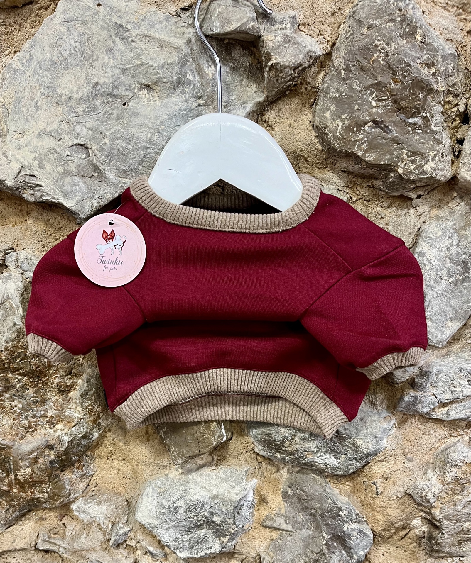 Camisola para cão borgonha com acabamentos bege pendurada numa cabide