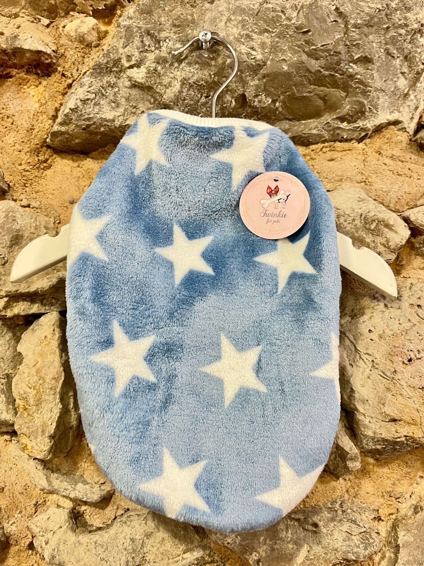 Roupa de cama para animal de estimação azul com estrelas brancas pendurada numa parede de pedra