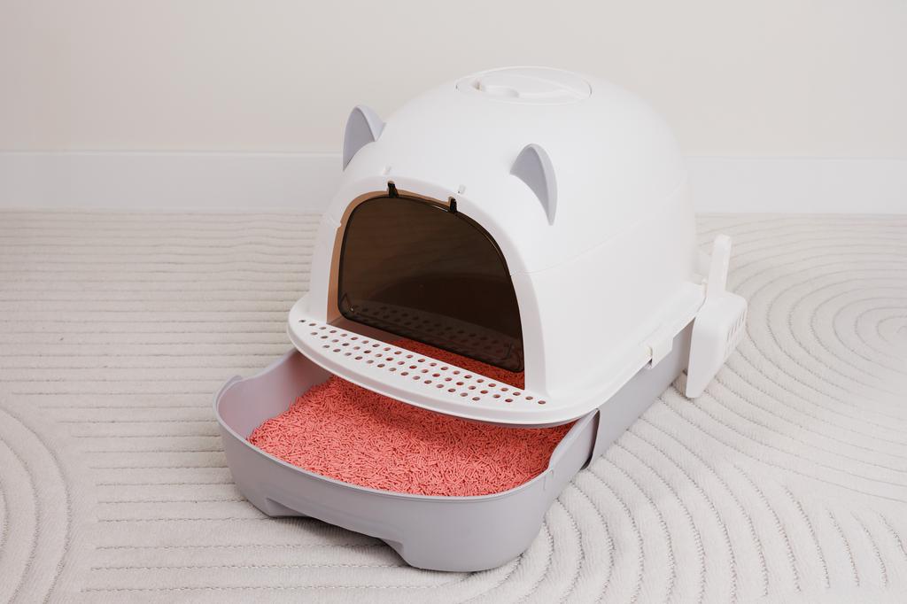 Caixa de areia para gatos em plástico branco e cinza com porta translúcida e areia rosa em bandeja inferior
