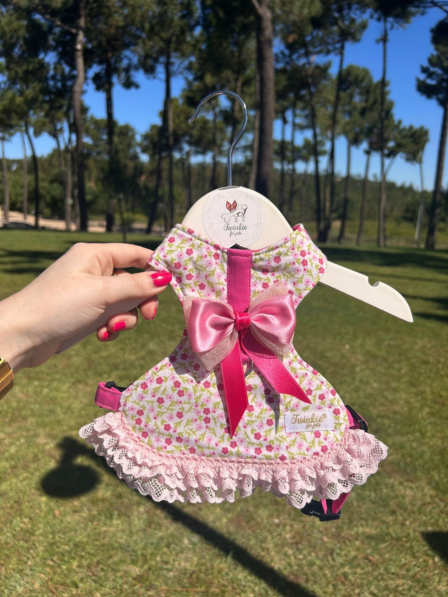 Vestido para cão rosa com padrão floral e laço em cabide branco ao ar livre