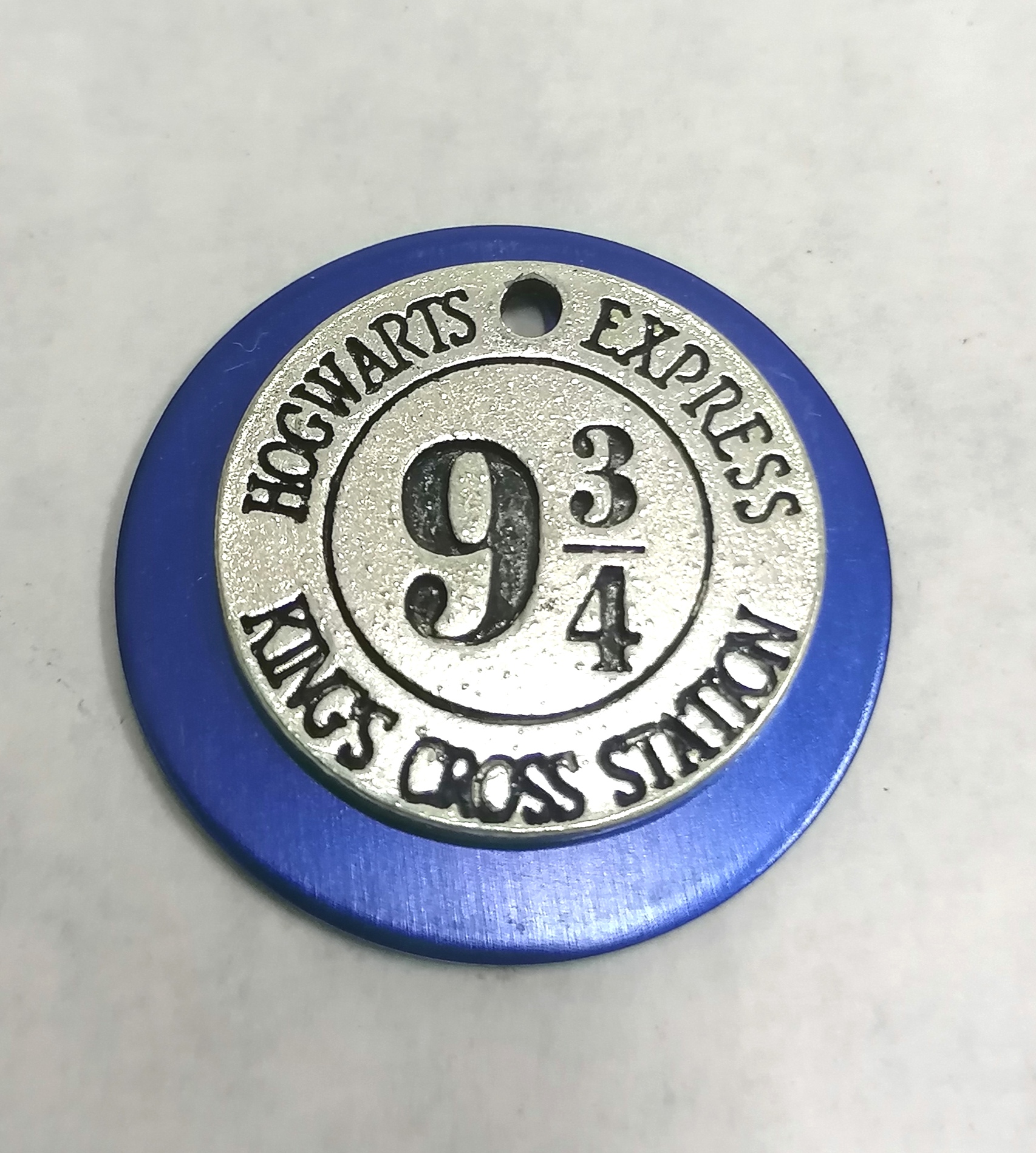 Chaveiro redondo azul e prateado com texto Hogwarts Express 9 3/4 Kings Cross Station