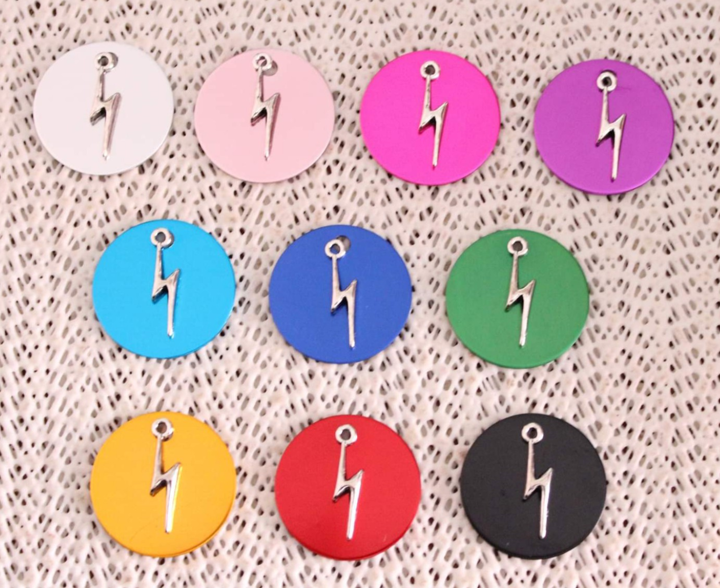 Dez medalhões coloridos circulares com um pingente de raio prateado sobre tecido bege entrelaçado