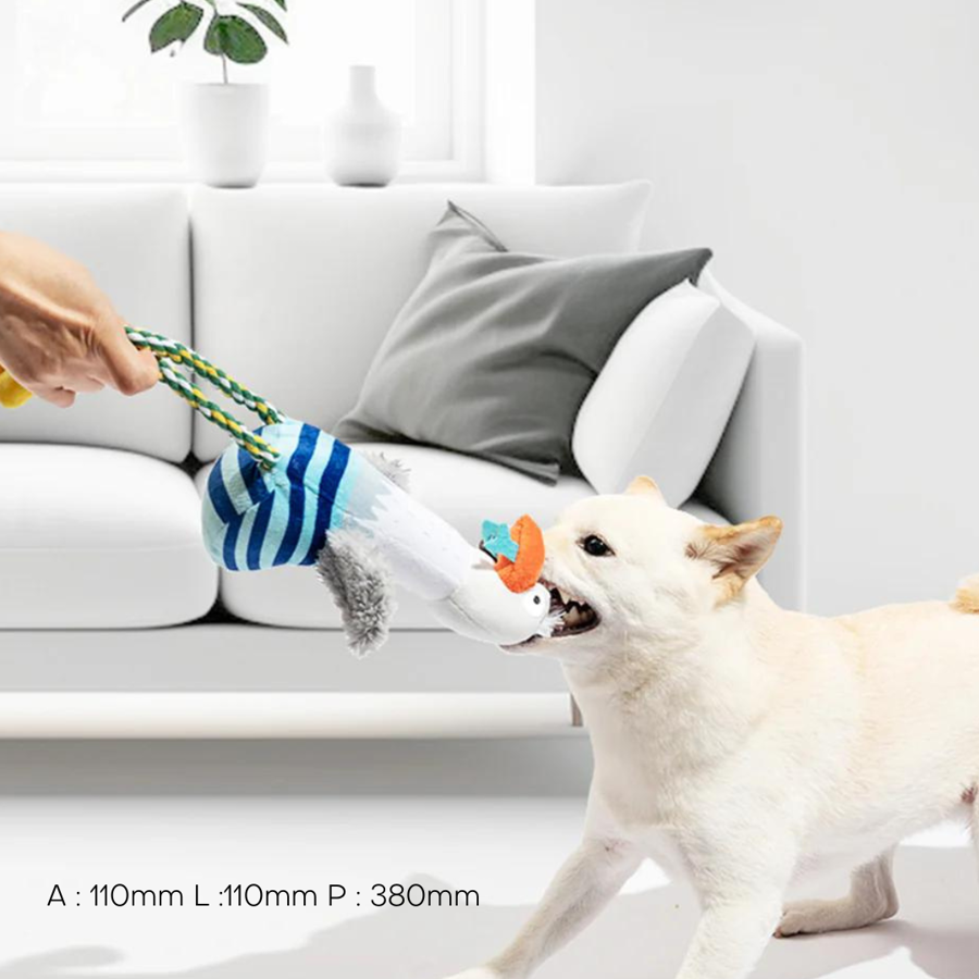 Brinquedo para cão em tecido com padrão riscado azul e branco e corda trançada, cão branco a brincar, interior com sofá branco e almofada cinza