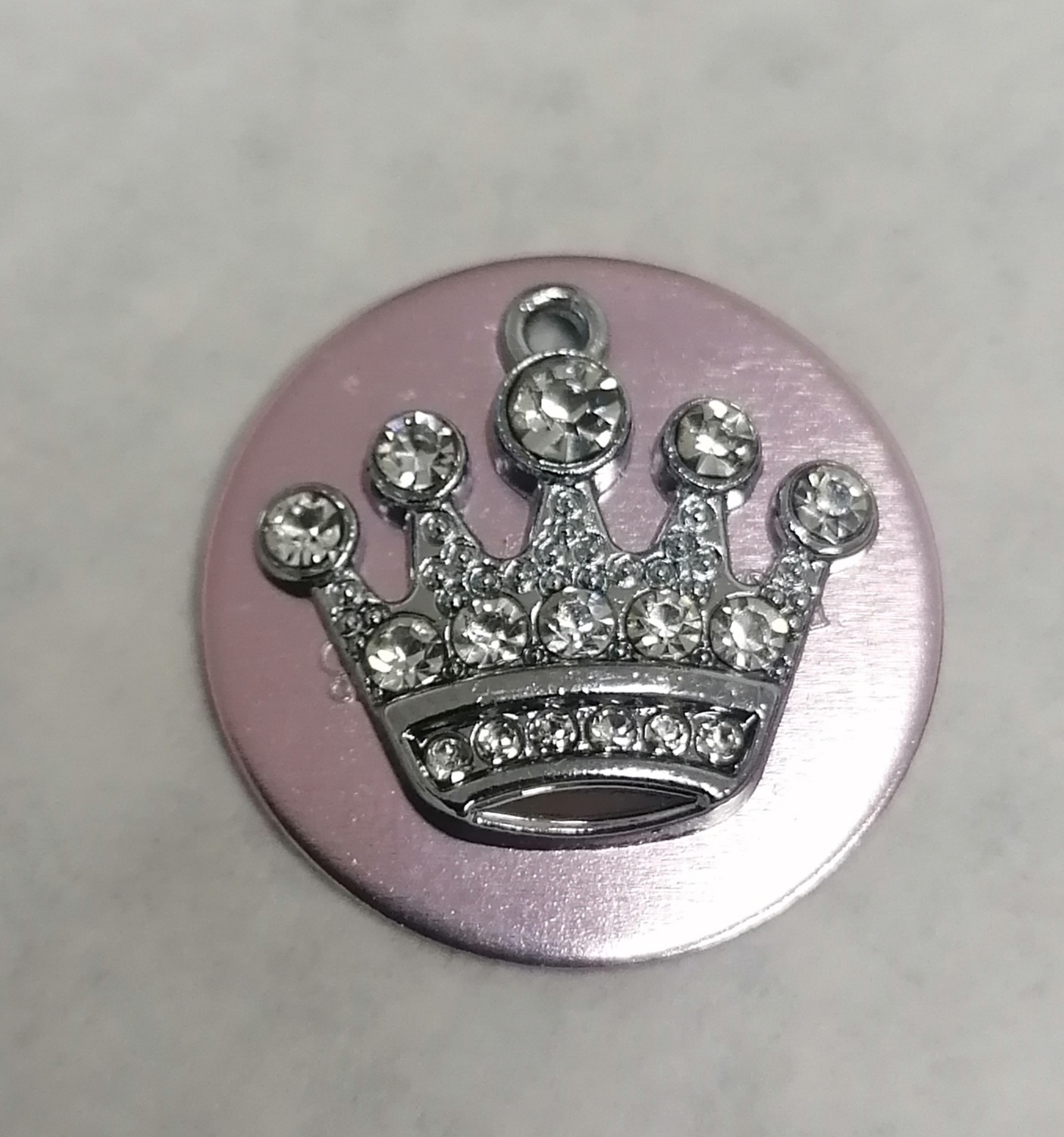 Medalha redonda cor de rosa com coroa prateada e pedras brilhantes