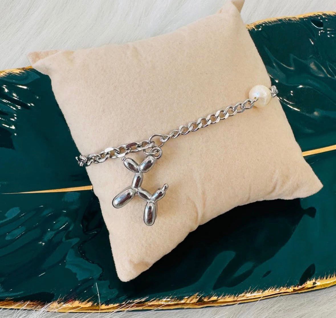 Pulseira metálica com pendente de balão de cão e pérola sobre almofada bege