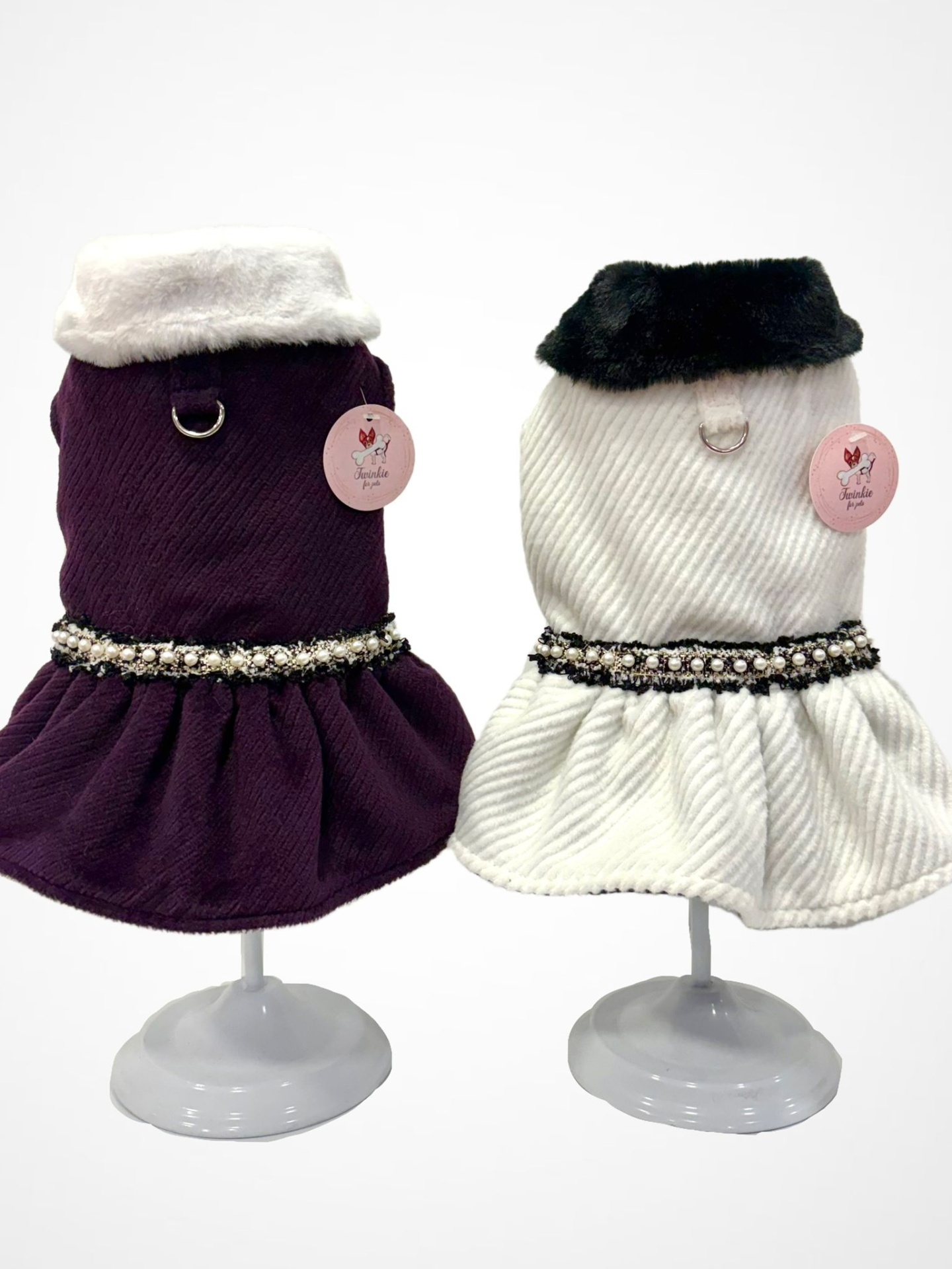 Dois vestidos para cães, um roxo com gola branca e outro branco com gola preta, com cintos de pérolas