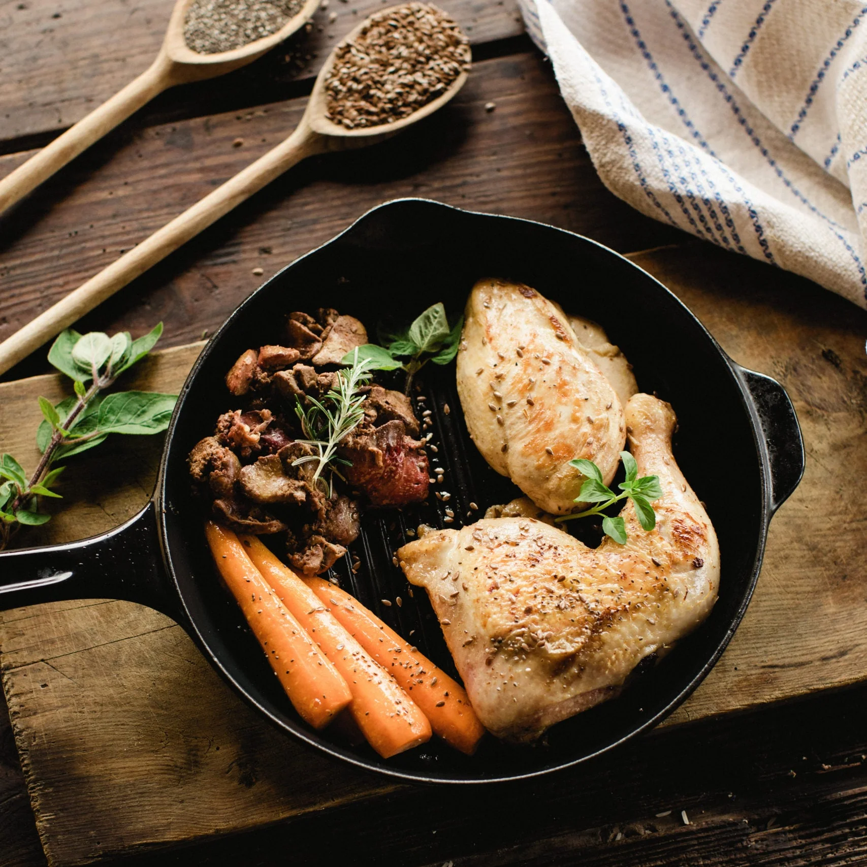 Frigideira com frango grelhado, carne, cenouras e ervas fresca sobre tábua de madeira