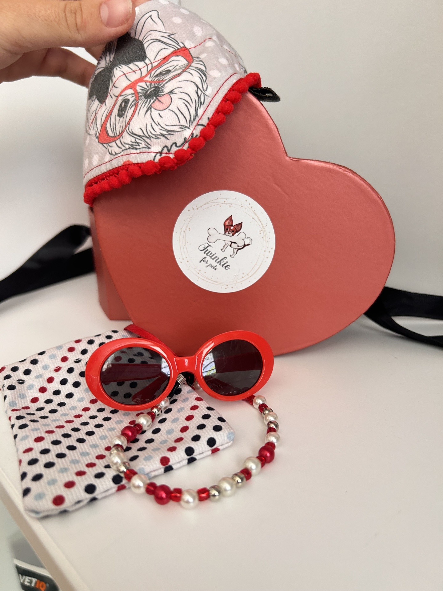 Caixa rosa em forma de coração com óculos de sol vermelhos, pulseira e saco de tecido com padrão de cão