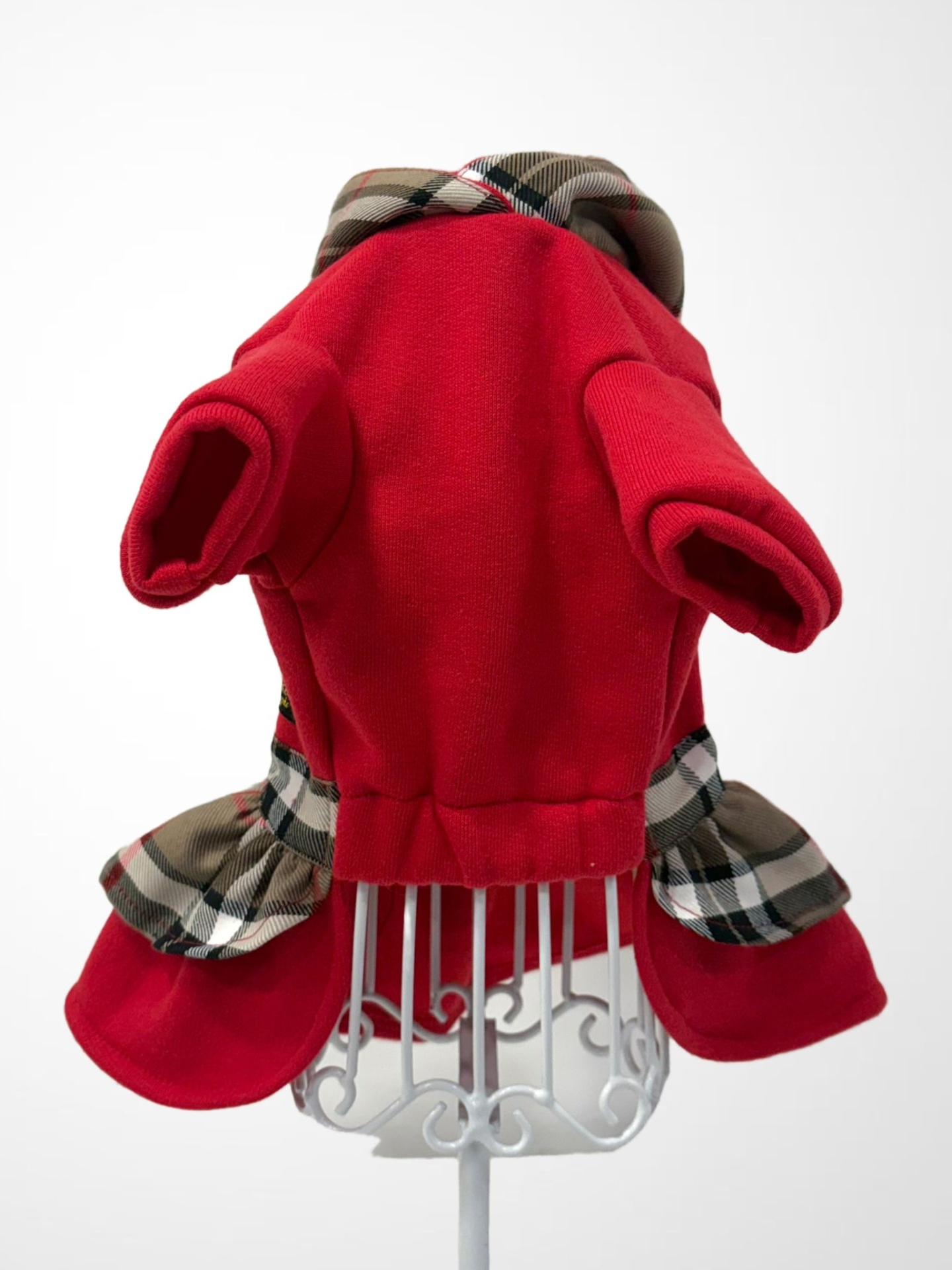 Casaco vermelho para cão com gola e barra xadrez num suporte metálico branco