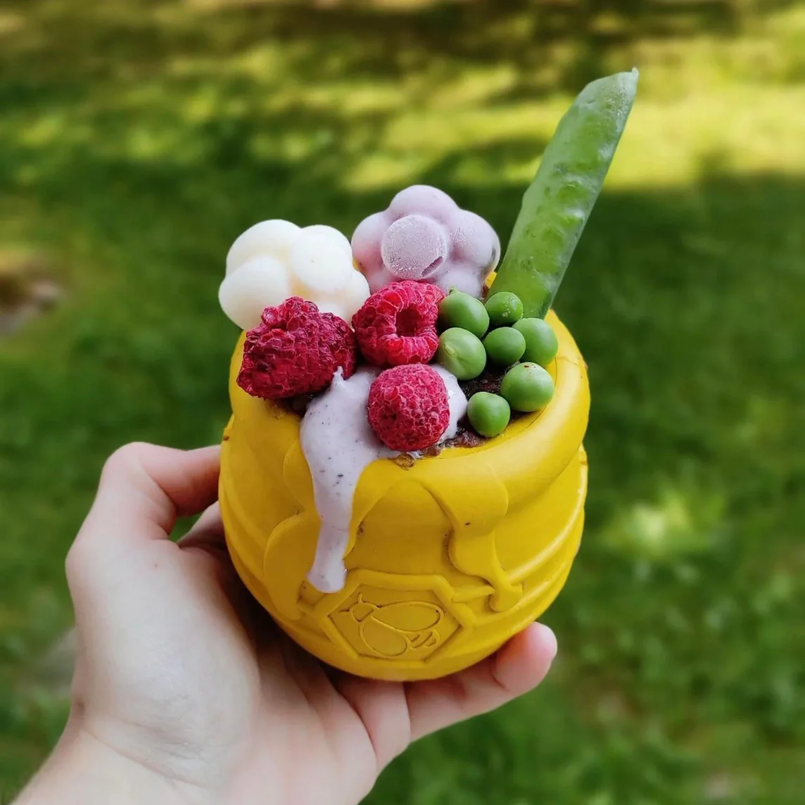 Vela amarela em formato de abelha com decoração de frutas e flores artificialmente coloridas.