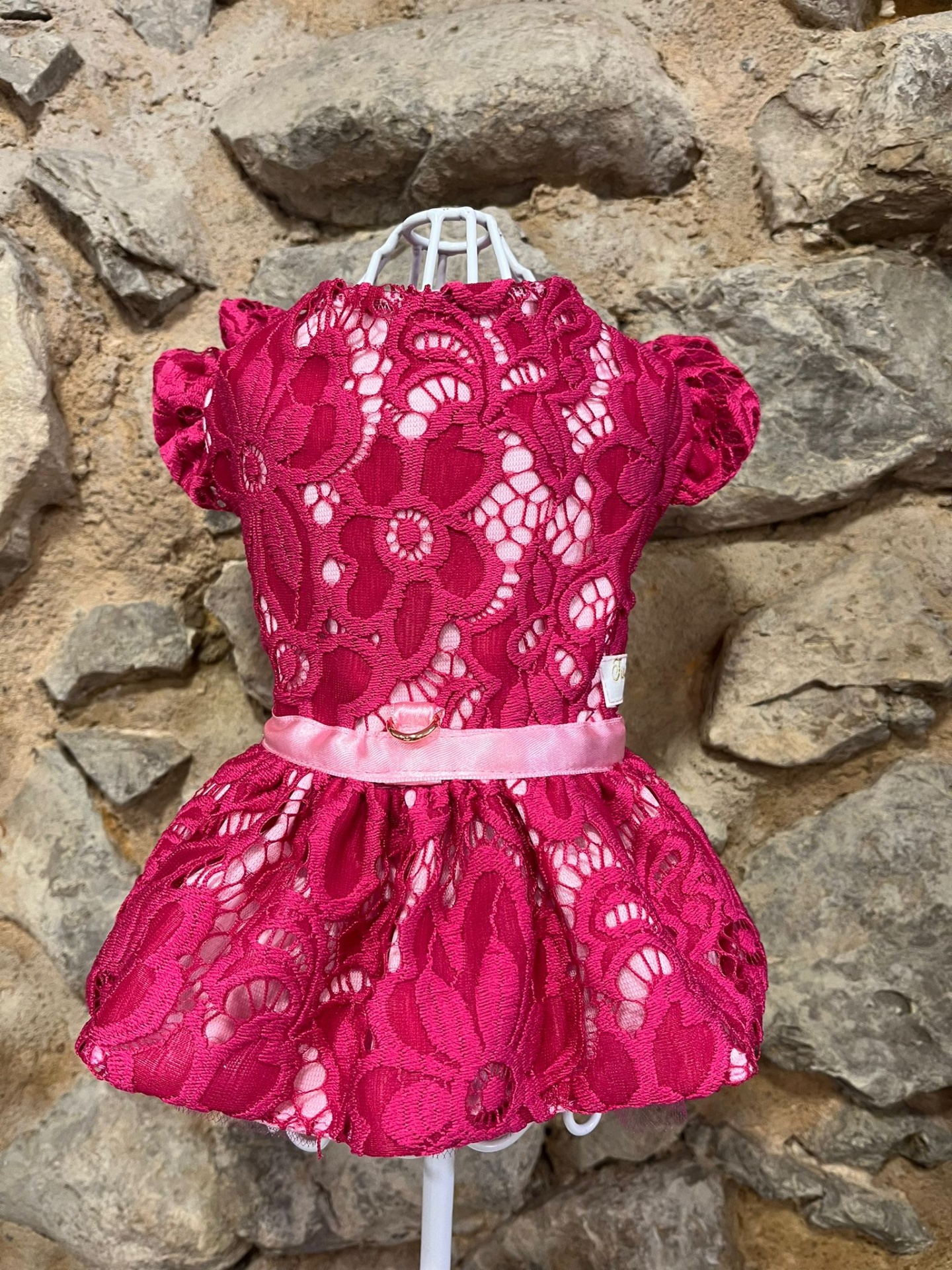 Vestido vermelho de renda floral com cinto rosa em manequim contra parede de pedra