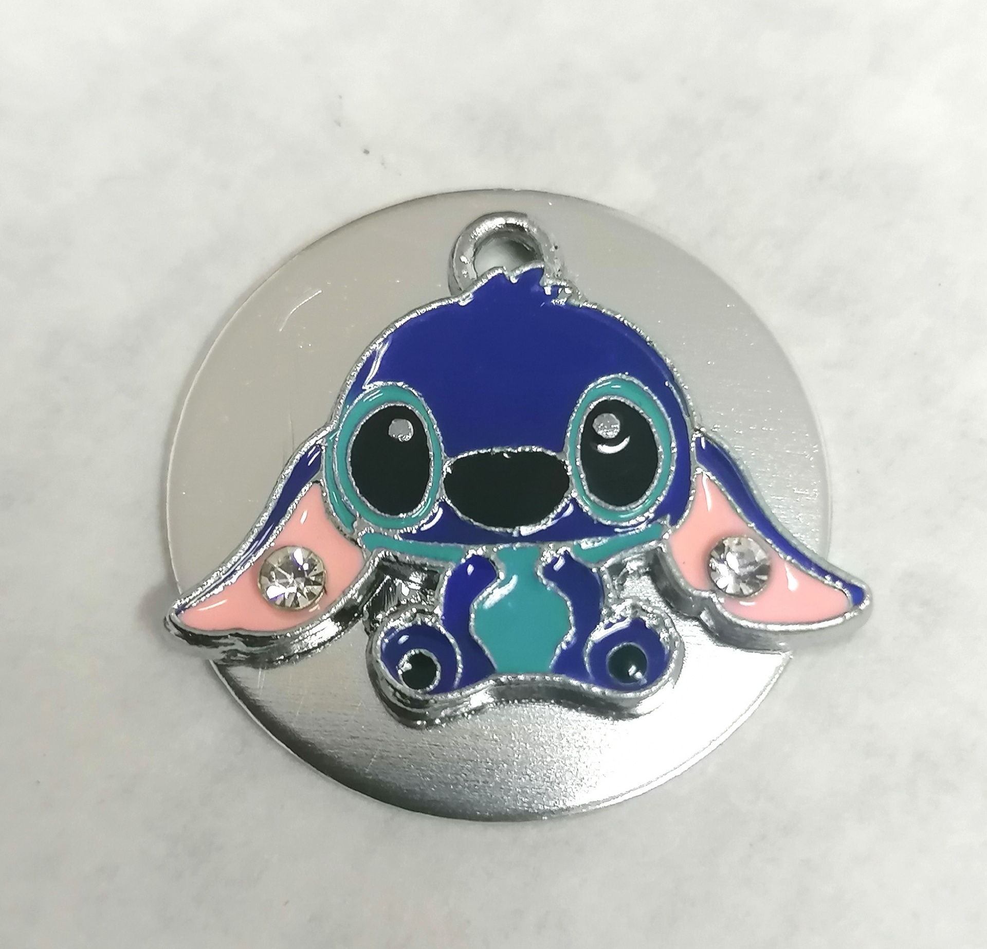 Pêndulo metálico prateado com personagem azul de olhos grandes e orelhas cor-de-rosa