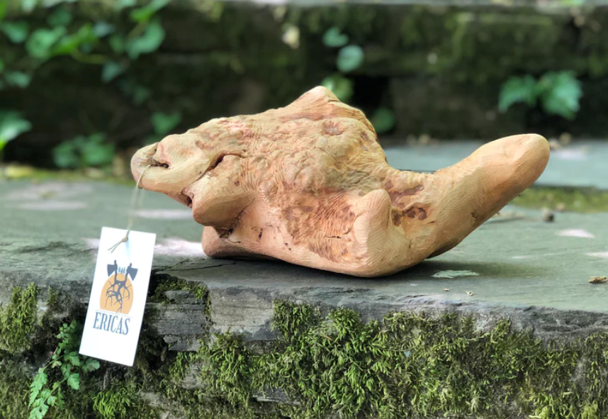 Escultura de madeira clara com etiqueta ERICAS sobre pedra musgosa