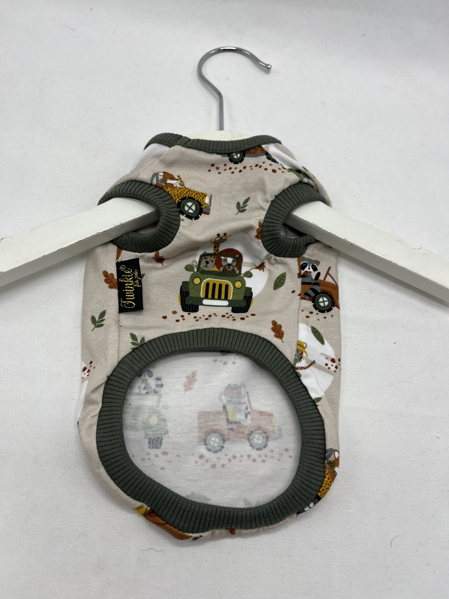 Roupa para cão bege com padrão de carrinhos e bordas verdes pendurada em cabide branco